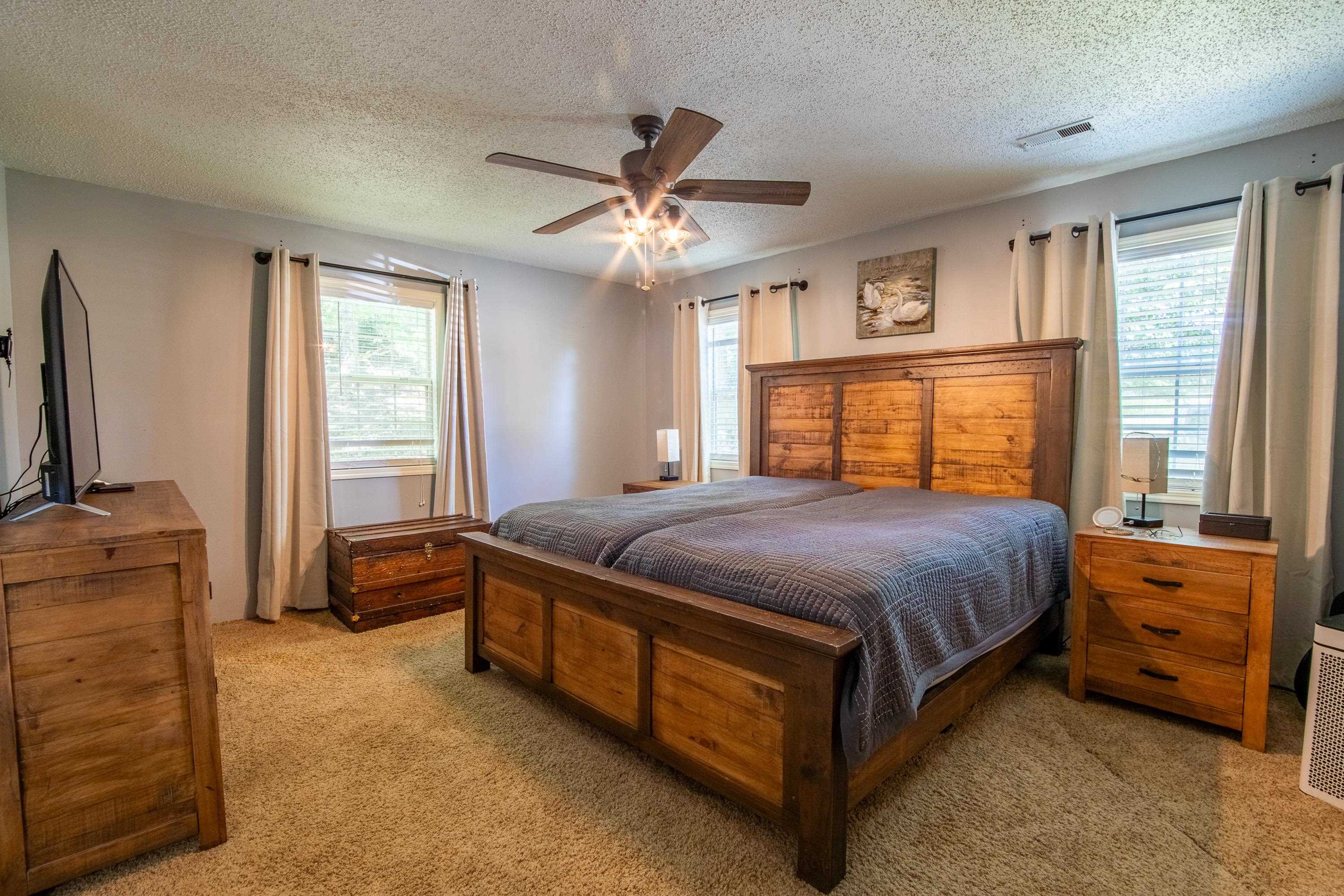 Carpeted bedroom featuring ceiling fan, multiple windows, and a textured ceiling