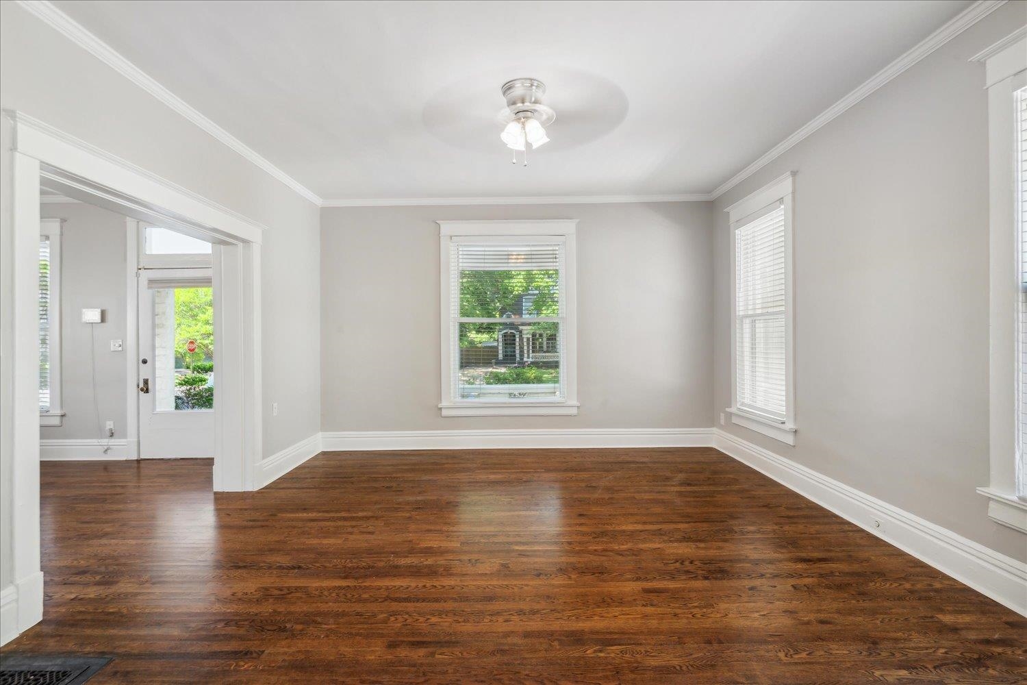 Large room with ornamental molding, dark wood flooring, and ceiling fan