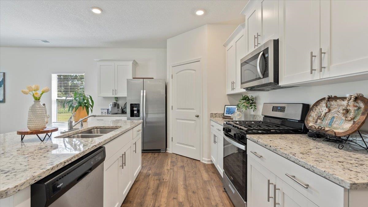 Kitchen featuring light stone counters, dark wood-type flooring, white cabinets, sink, and appliances with stainless steel finishes