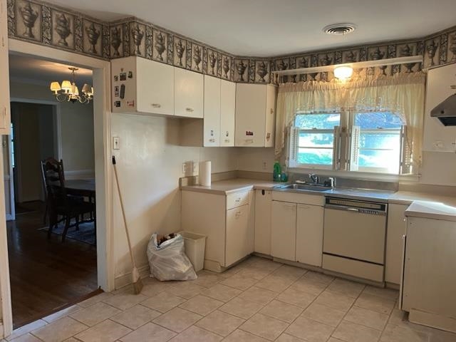 Kitchen with light tile flooring, dishwasher, a notable chandelier, white cabinetry, and sink