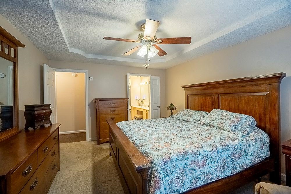 Bedroom with carpet, ceiling fan, a tray ceiling, connected bathroom