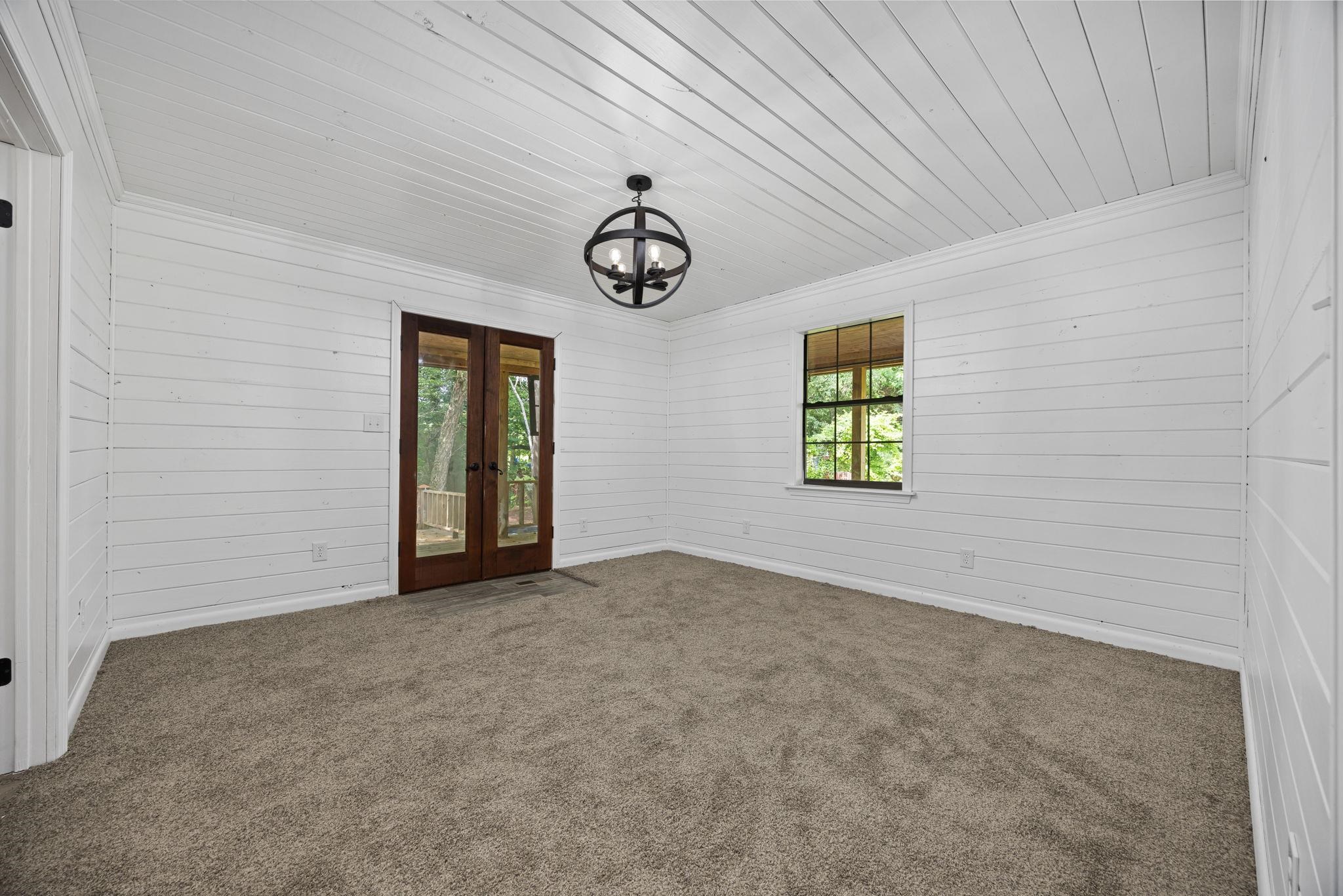 Carpeted empty room featuring french doors, crown molding, an inviting chandelier, and wooden ceiling