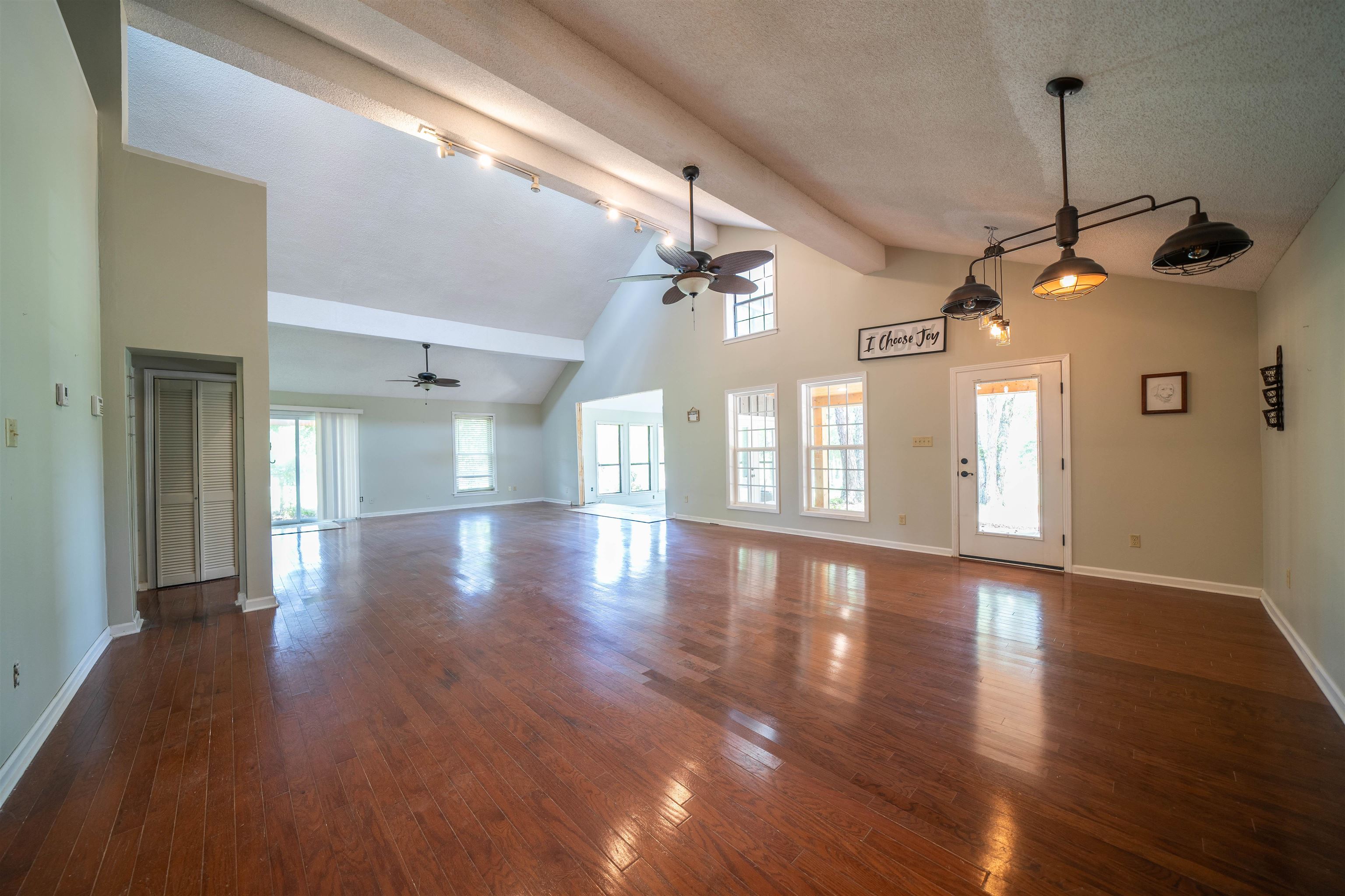 Unfurnished living room featuring track lighting, ceiling fan, dark wood-type flooring, high vaulted ceiling, and beamed ceiling