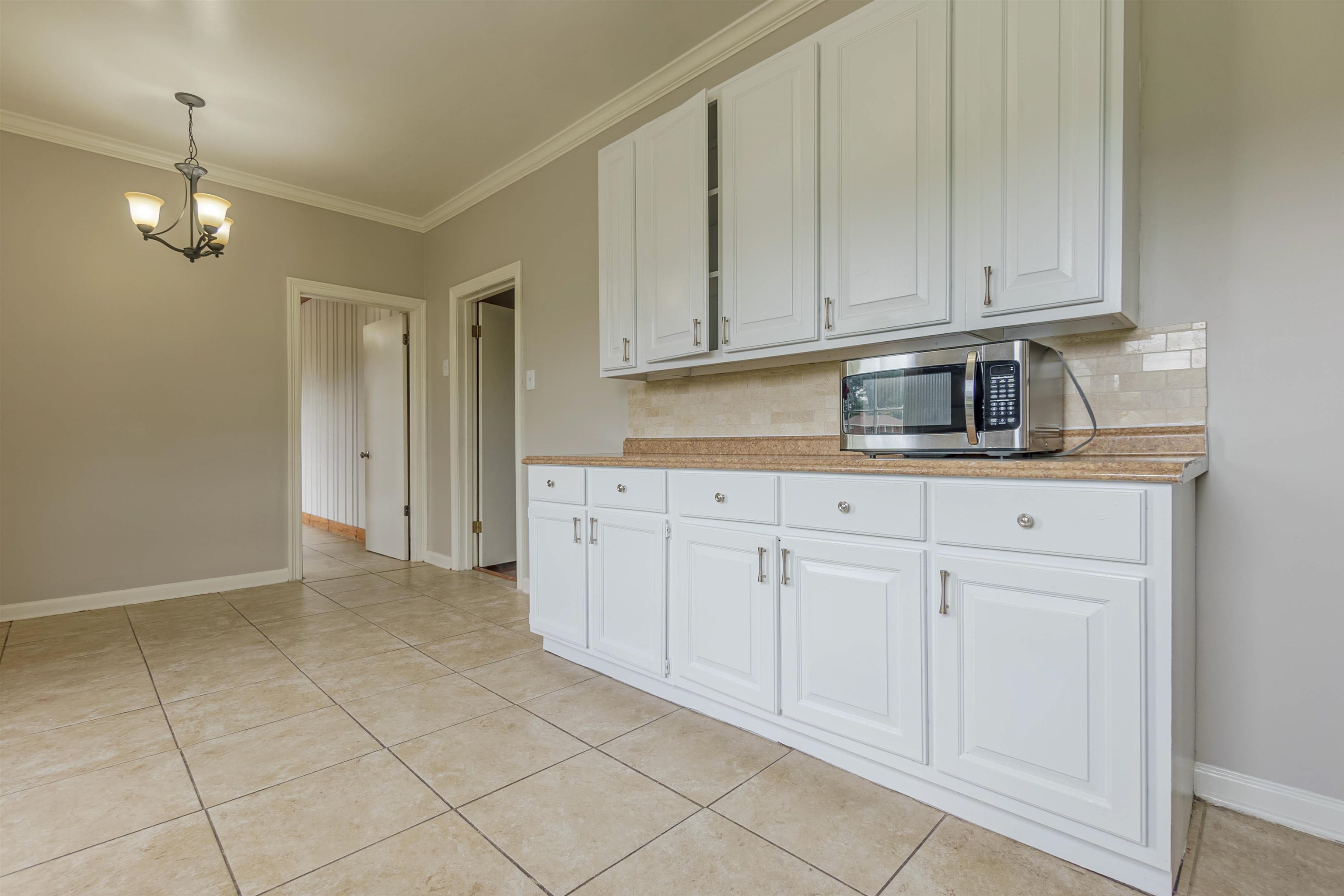 Kitchen featuring decorative light fixtures, white cabinets, backsplash, and crown molding