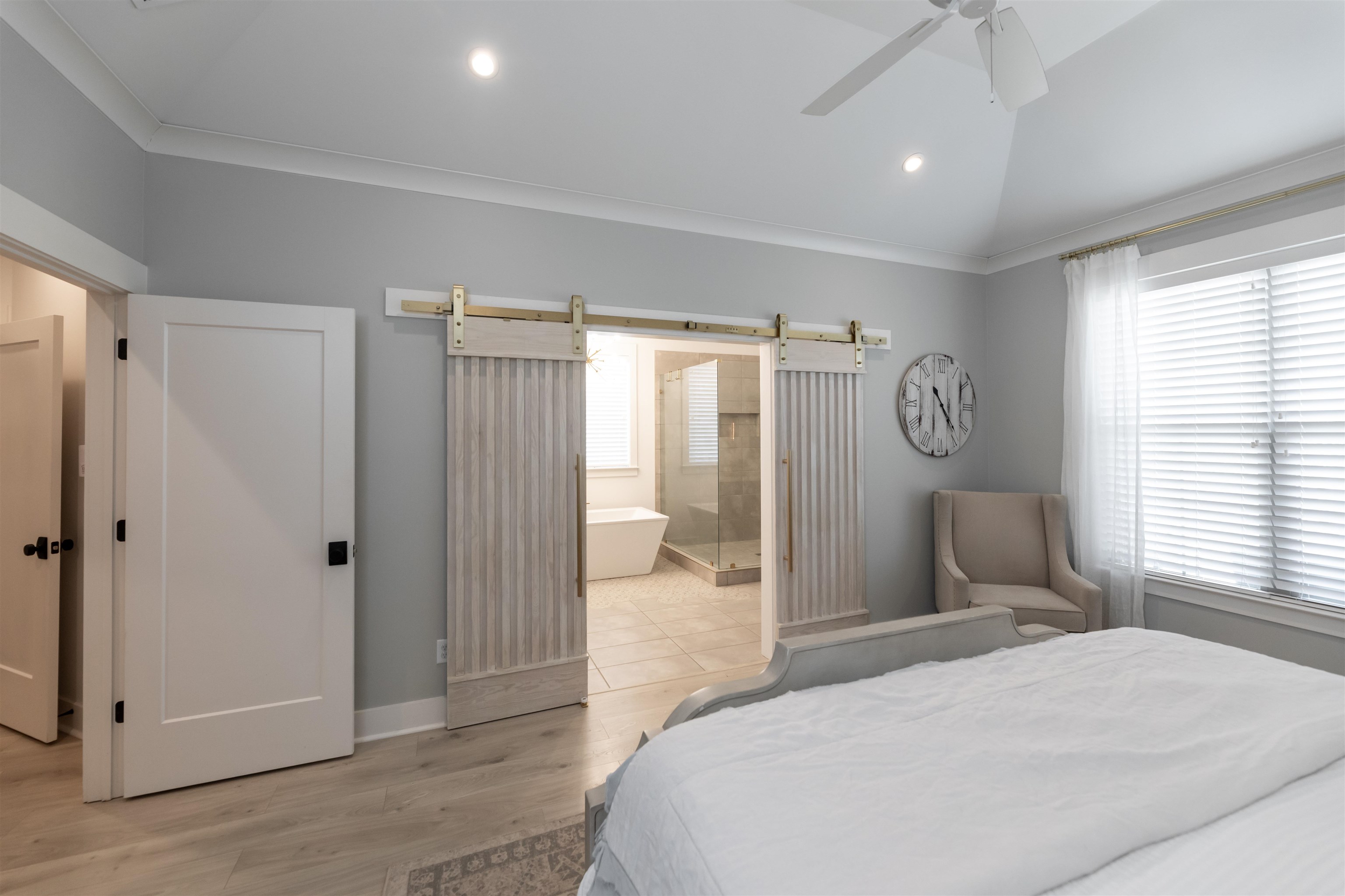 Bedroom with ceiling fan, light hardwood / wood-style floors, ensuite bath, a barn door, and lofted ceiling