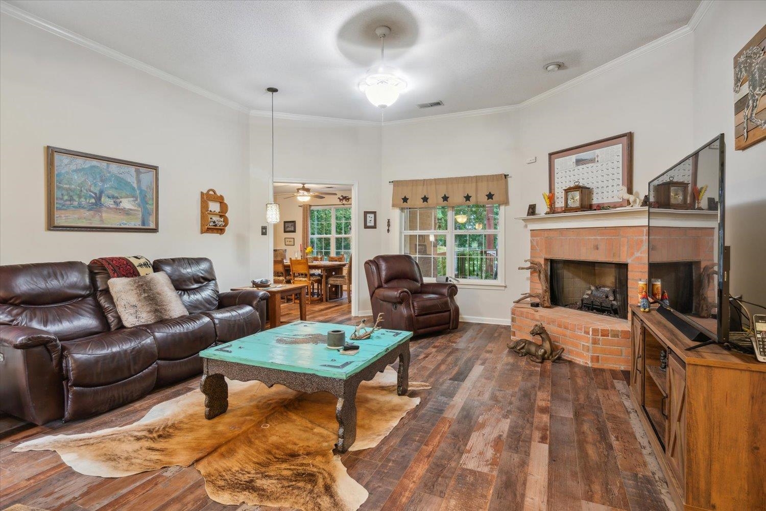 Living room featuring a brick fireplace, ceiling fan, crown molding, and dark wood-type flooring