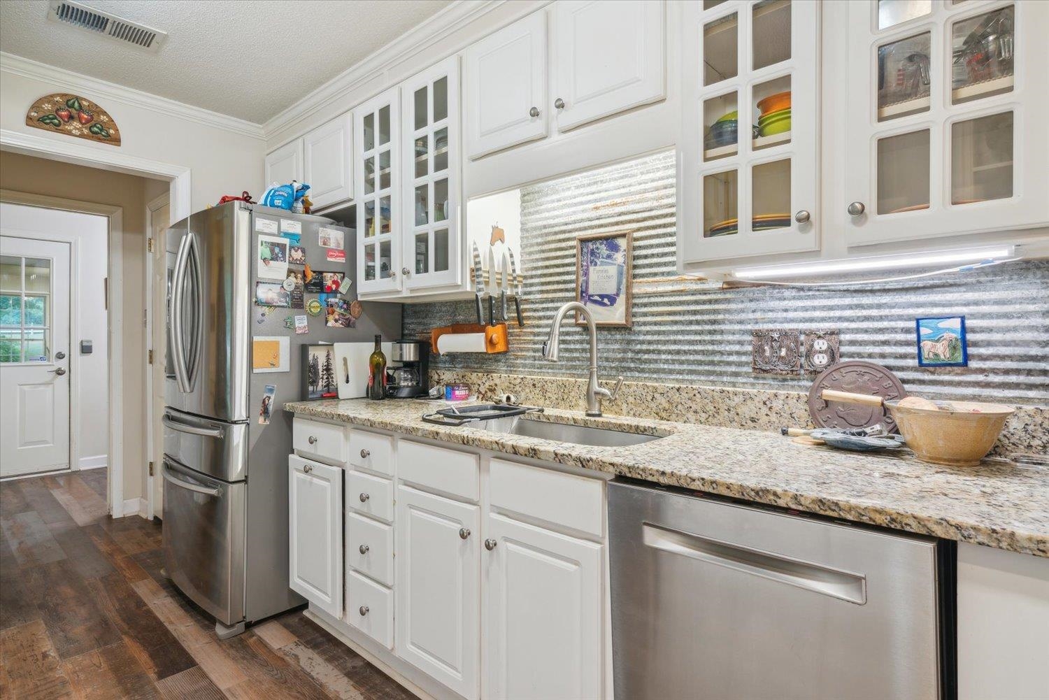 Kitchen featuring dark hardwood / wood-style flooring, tasteful backsplash, crown molding, white cabinets, and appliances with stainless steel finishes