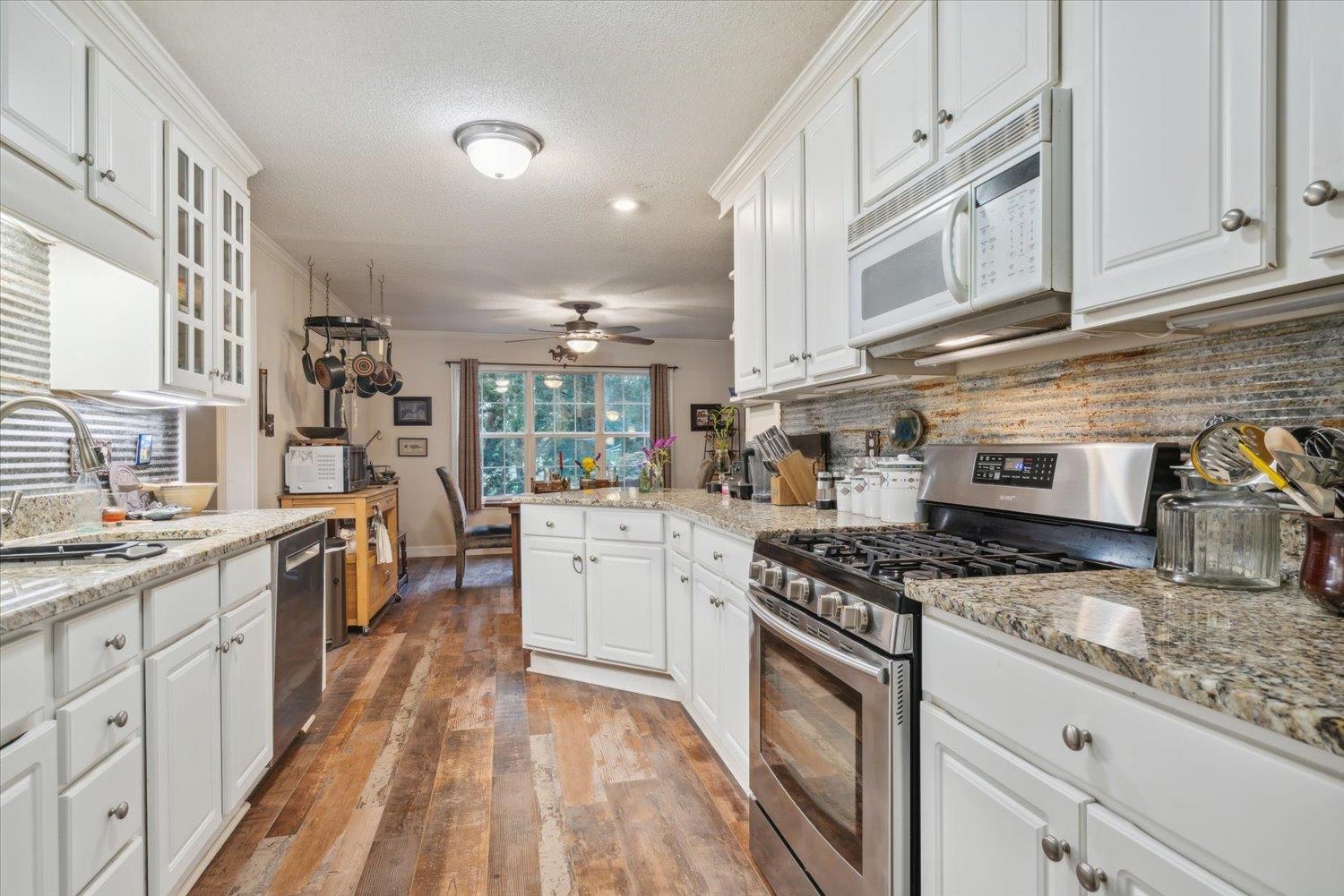Kitchen featuring stainless steel appliances, ceiling fan, white cabinetry, and tasteful backsplash