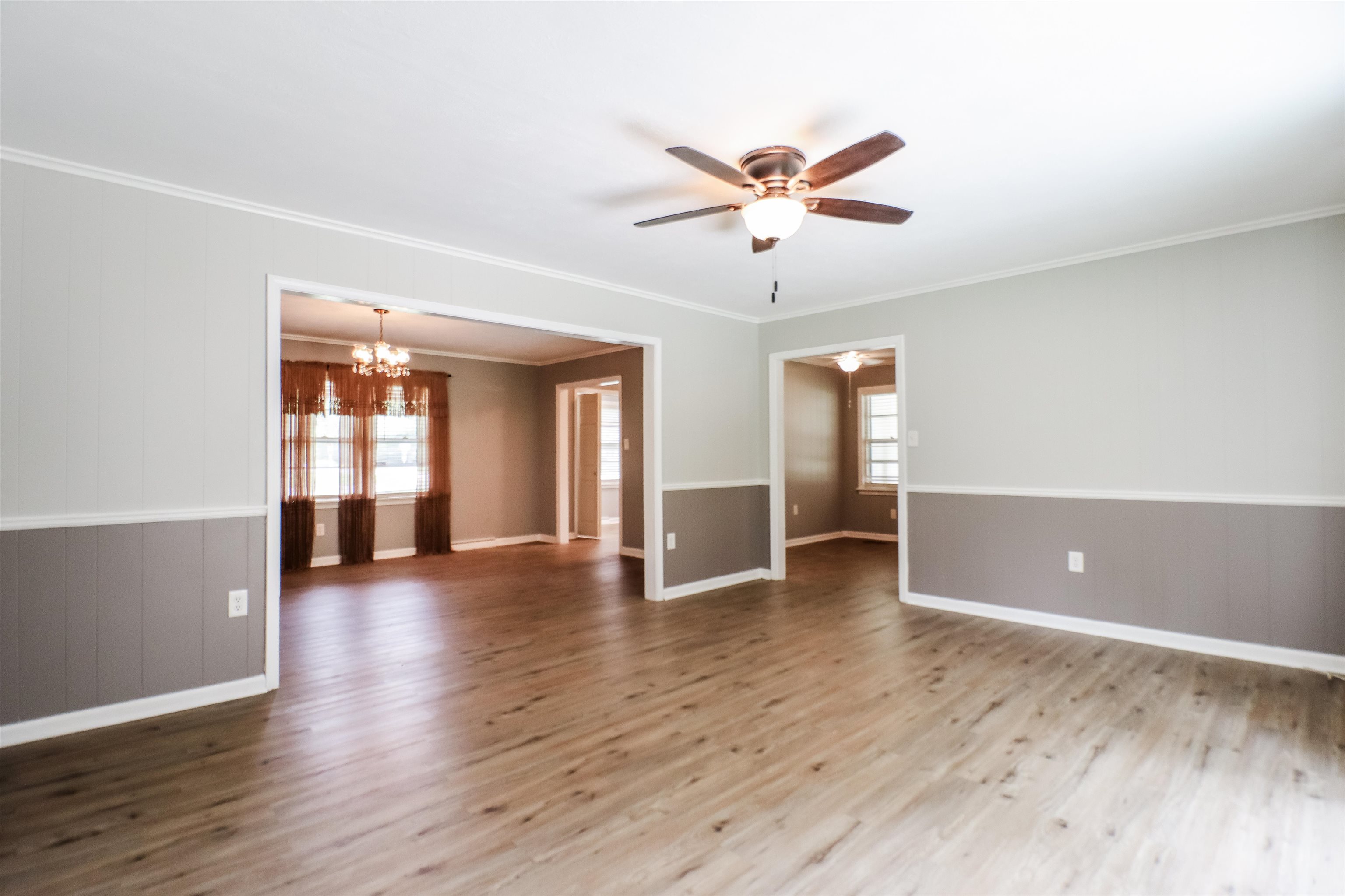 Spare room featuring plenty of natural light, ceiling fan with notable chandelier, crown molding, and wood-type flooring