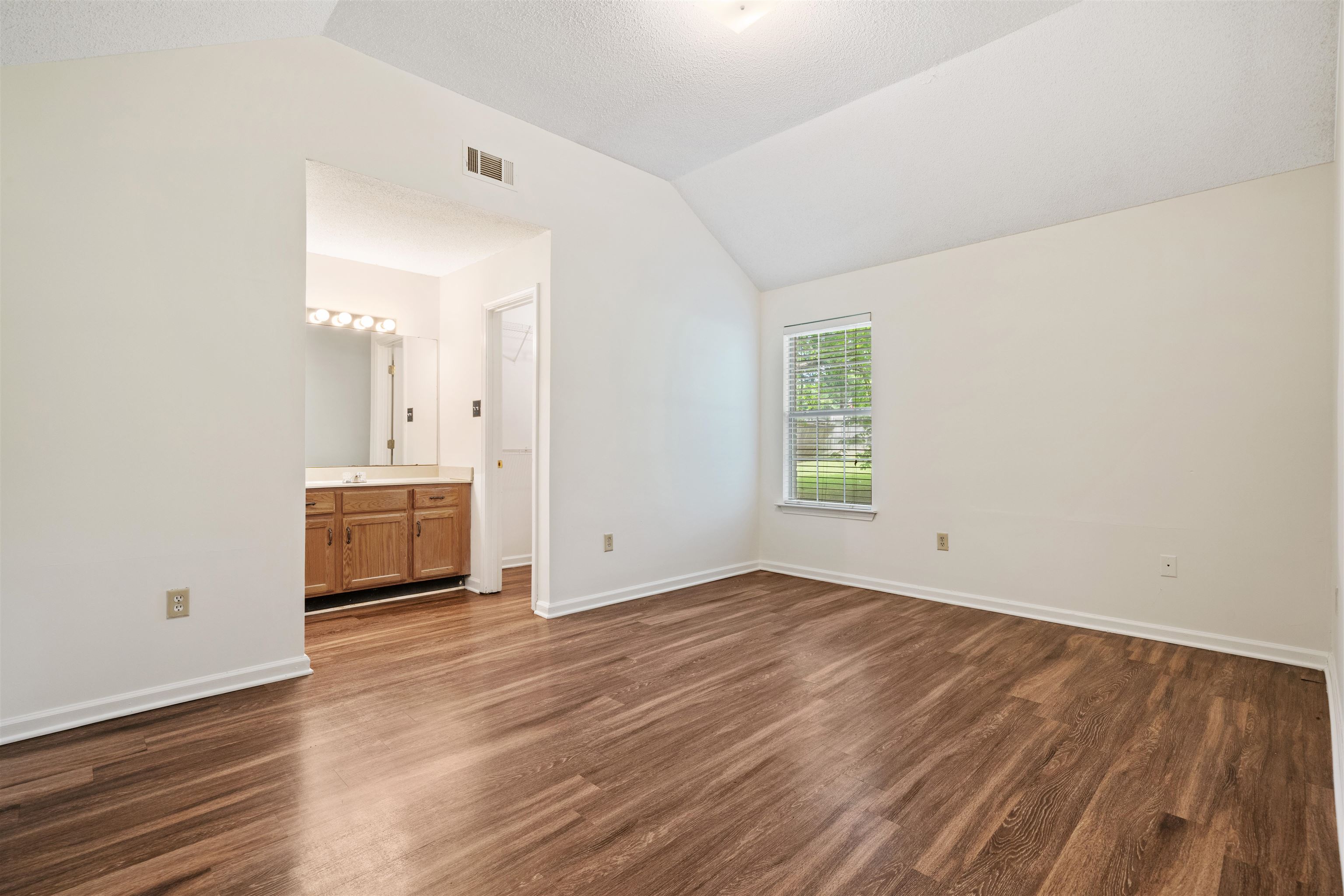 Primary Bedroom featuring lofted ceiling, wood-type flooring, and connected bathroom