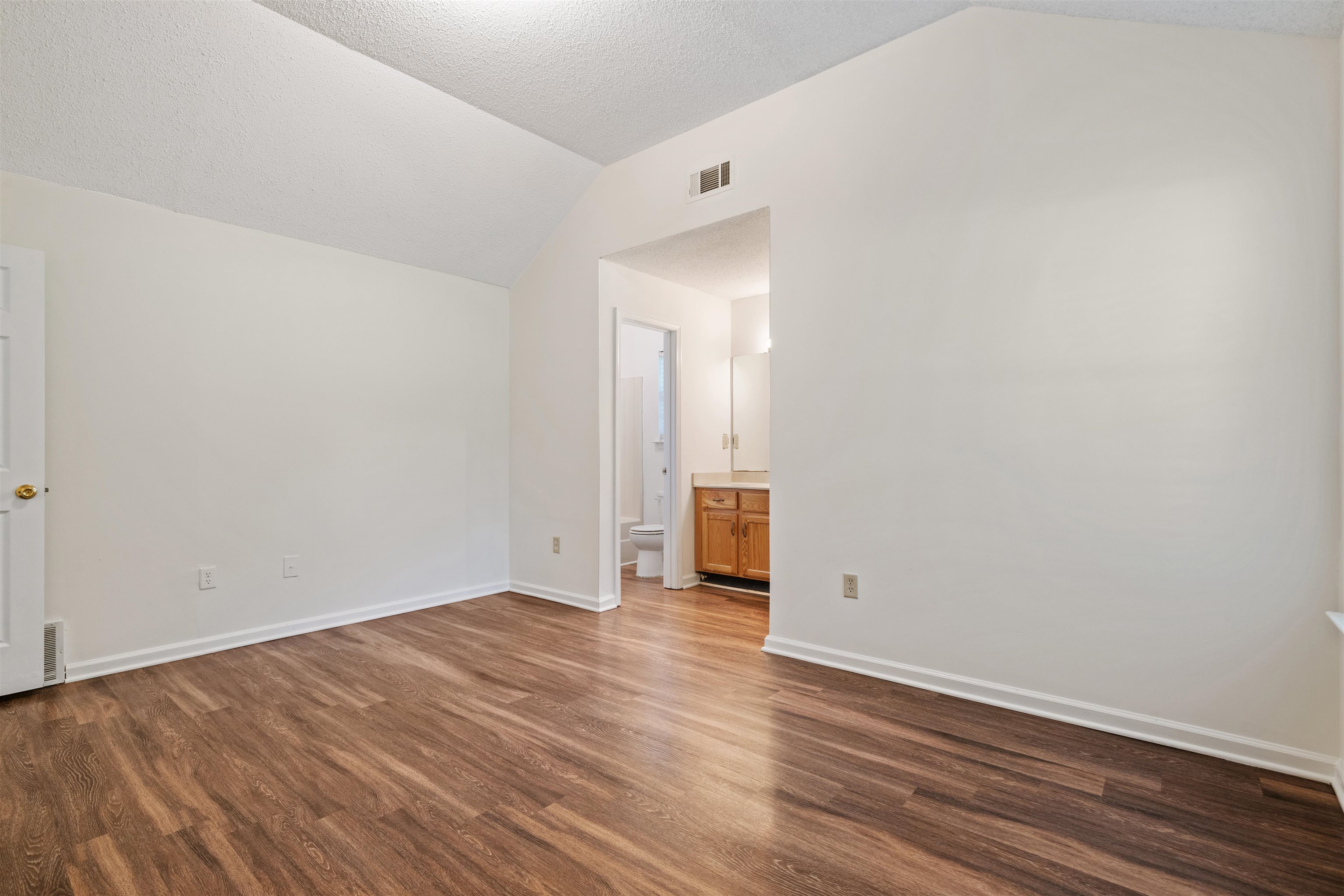 Primary bedroom with a spray textured ceiling, connected bathroom, hardwood / wood-style floors, and vaulted ceiling