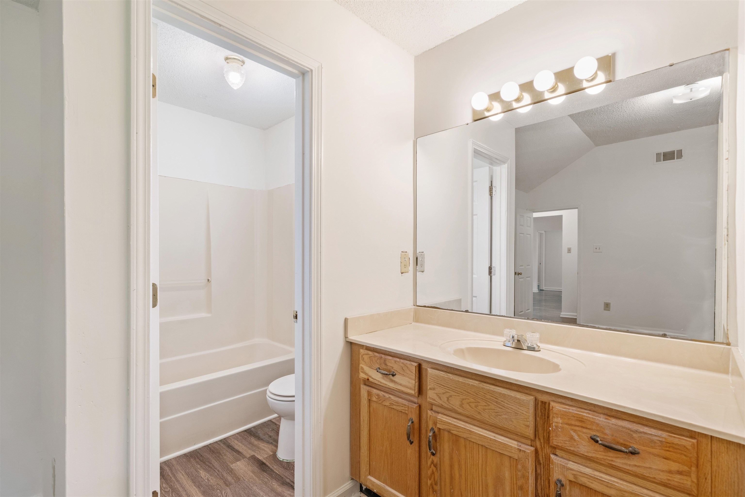 Primary bathroom featuring vanity, hardwood / wood-style flooring, washtub / shower combination, toilet, and sprayed ceiling