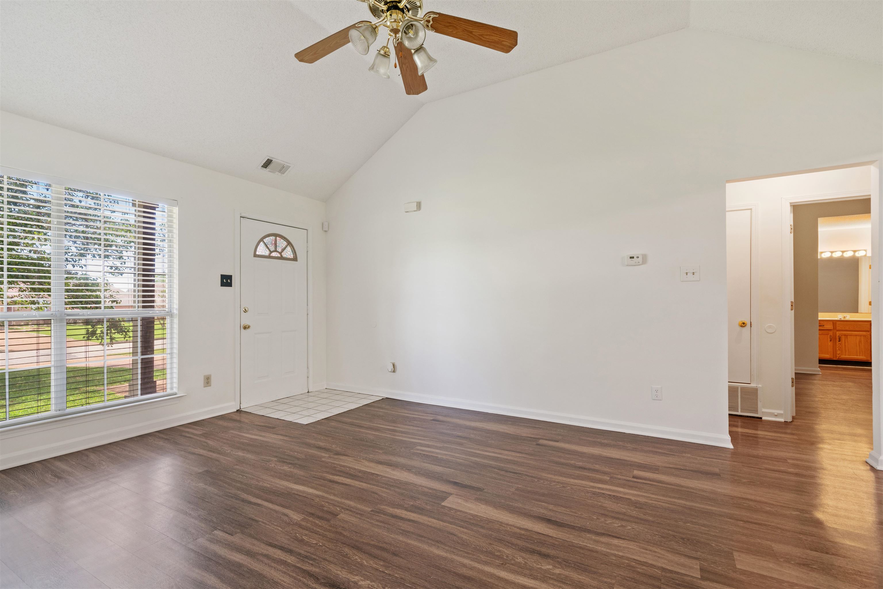 Entry area with tile apron and Living Room with ceiling fan, high vaulted ceiling, and dark wood-type flooring