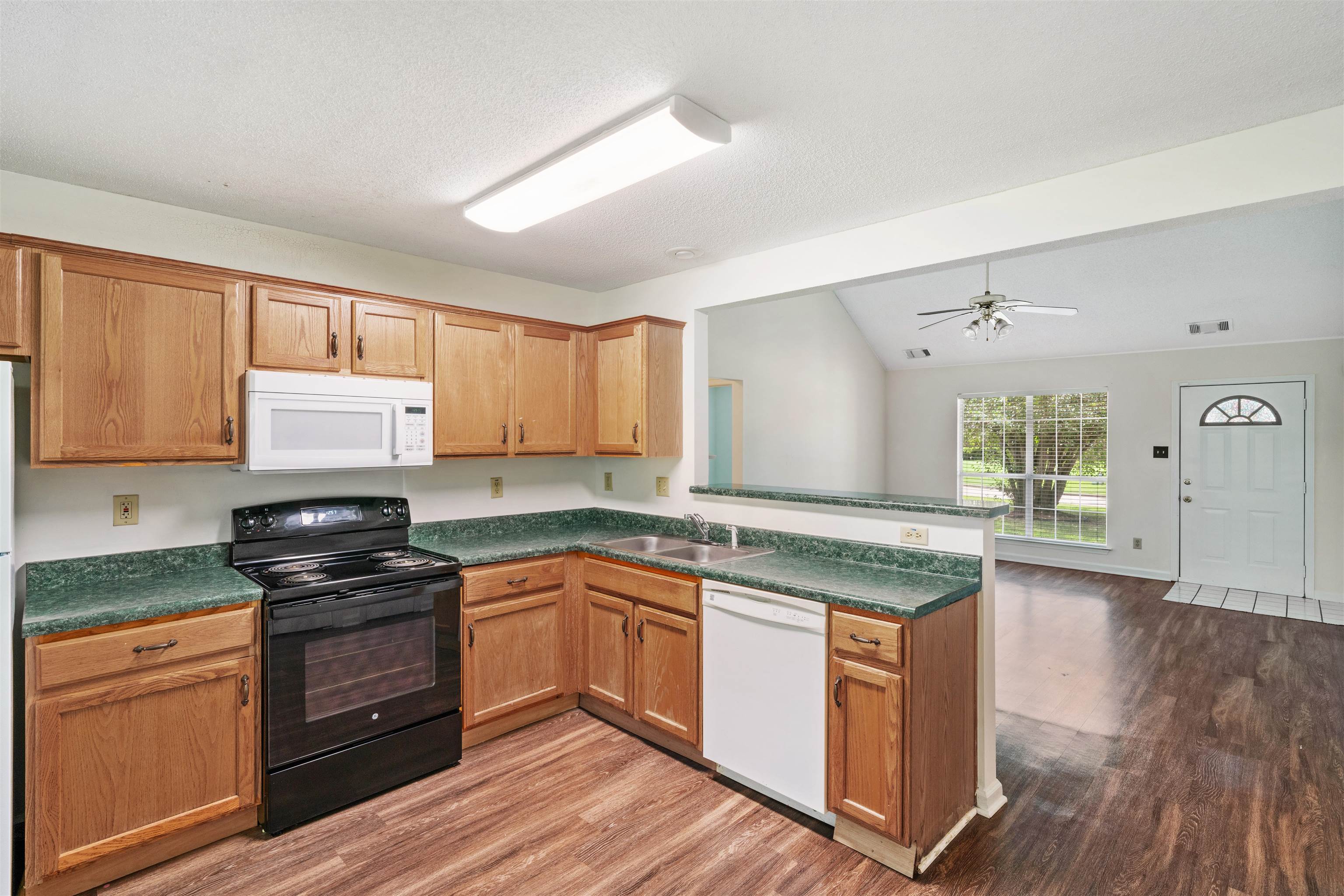 Kitchen with hardwood / wood-style floors, sprayed ceiling, white appliances, and kitchen peninsula with bartop.
