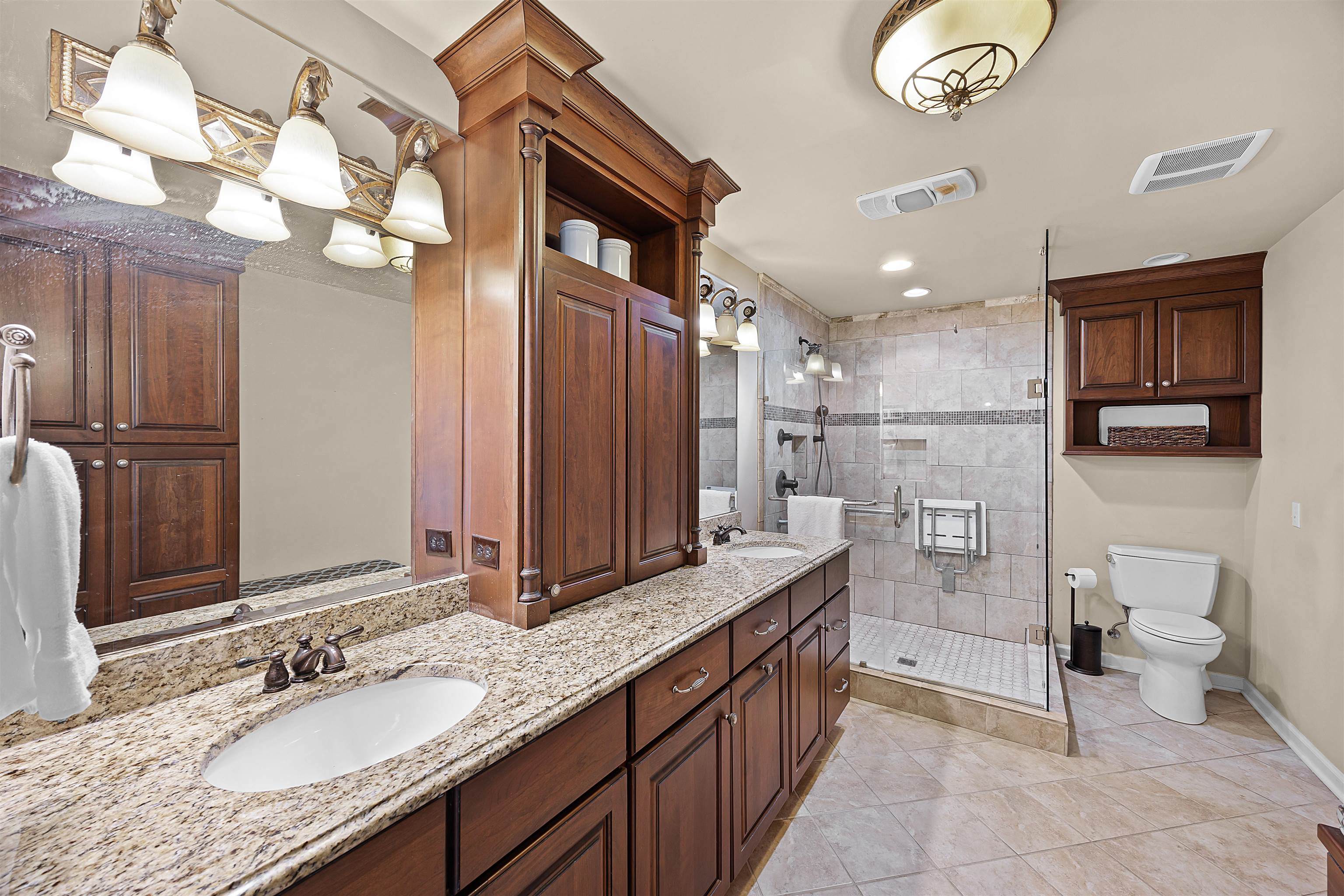 Bathroom featuring dual sinks, vanity with extensive cabinet space, a tile shower with door, & tile floors