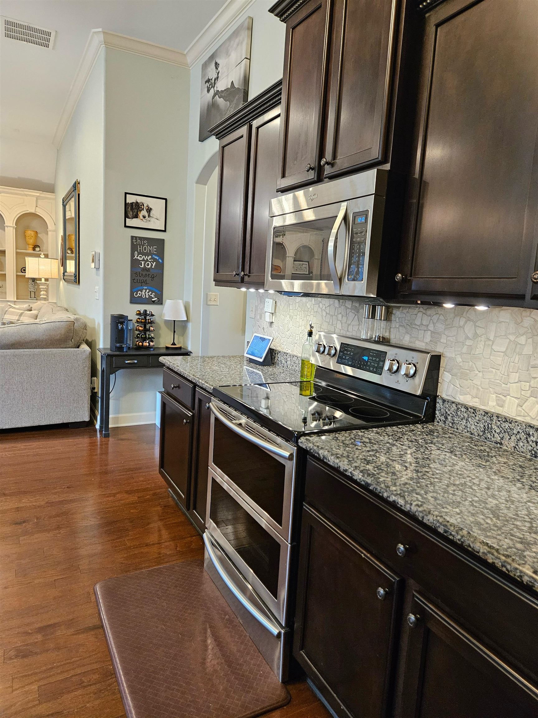 Kitchen with appliances with stainless steel finishes, stove with double ovens, microwave, dishwasher, kitchen island with sink and breakfast bar with pendant lighting, hardwood flooring, and adjoining breakfast / dining area.