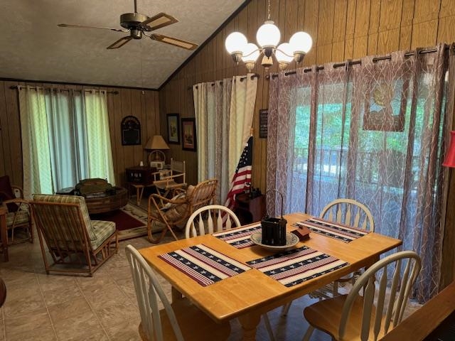 Dining room with wood walls, tile patterned floors, ceiling fan with notable chandelier, and vaulted ceiling