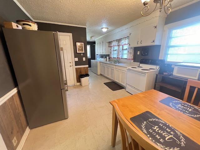 Kitchen featuring white cabinetry, light tile patterned floors, white electric range, stainless steel fridge, and plenty of natural light