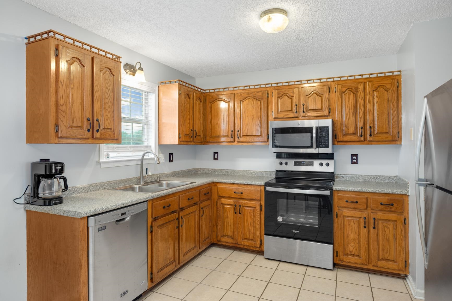 Kitchen featuring sink, a textured ceiling, light tile patterned floors, and stainless steel appliances