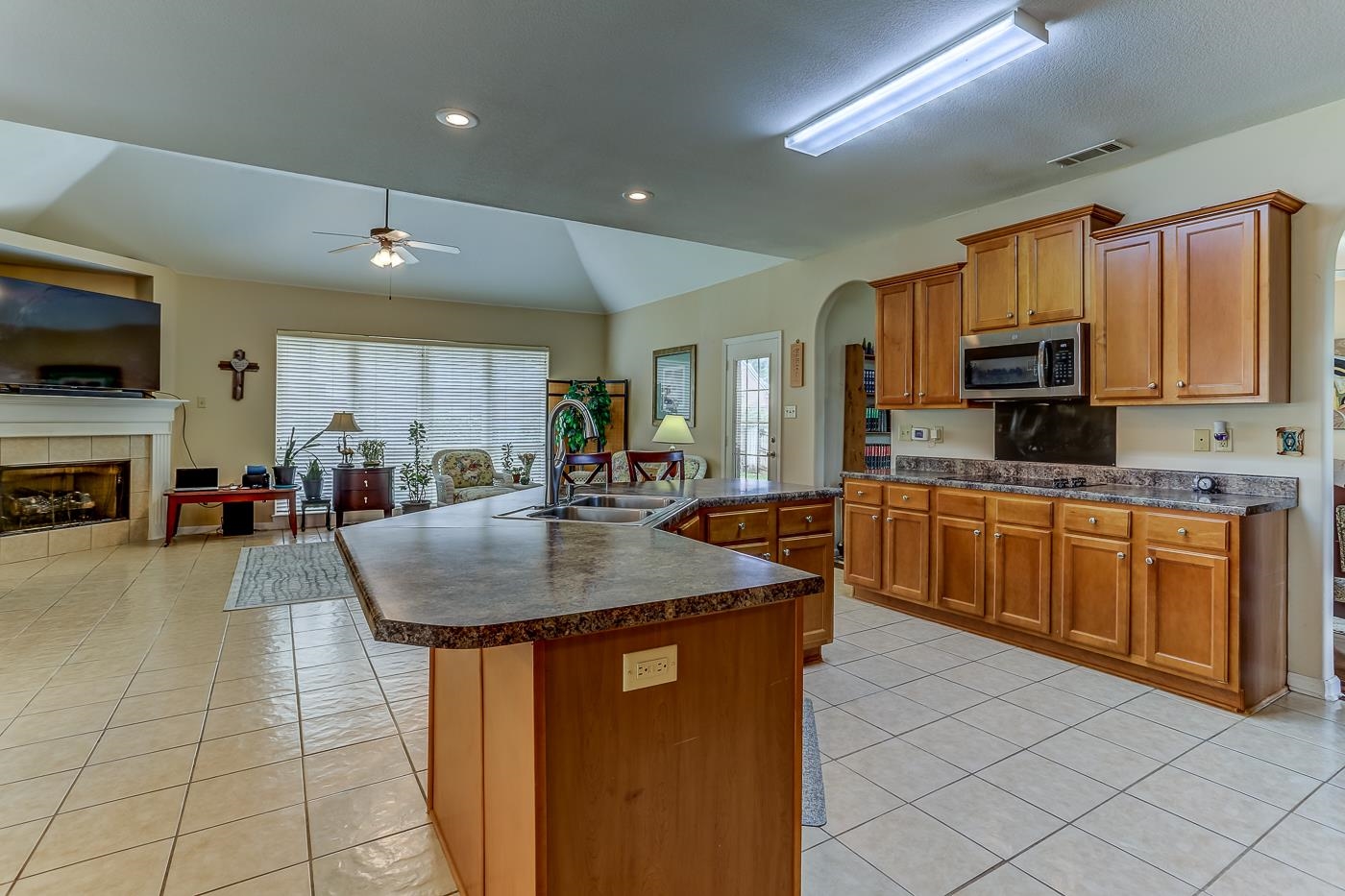 Kitchen featuring sink, a tile fireplace, a kitchen island with sink, lofted ceiling, and ceiling fan