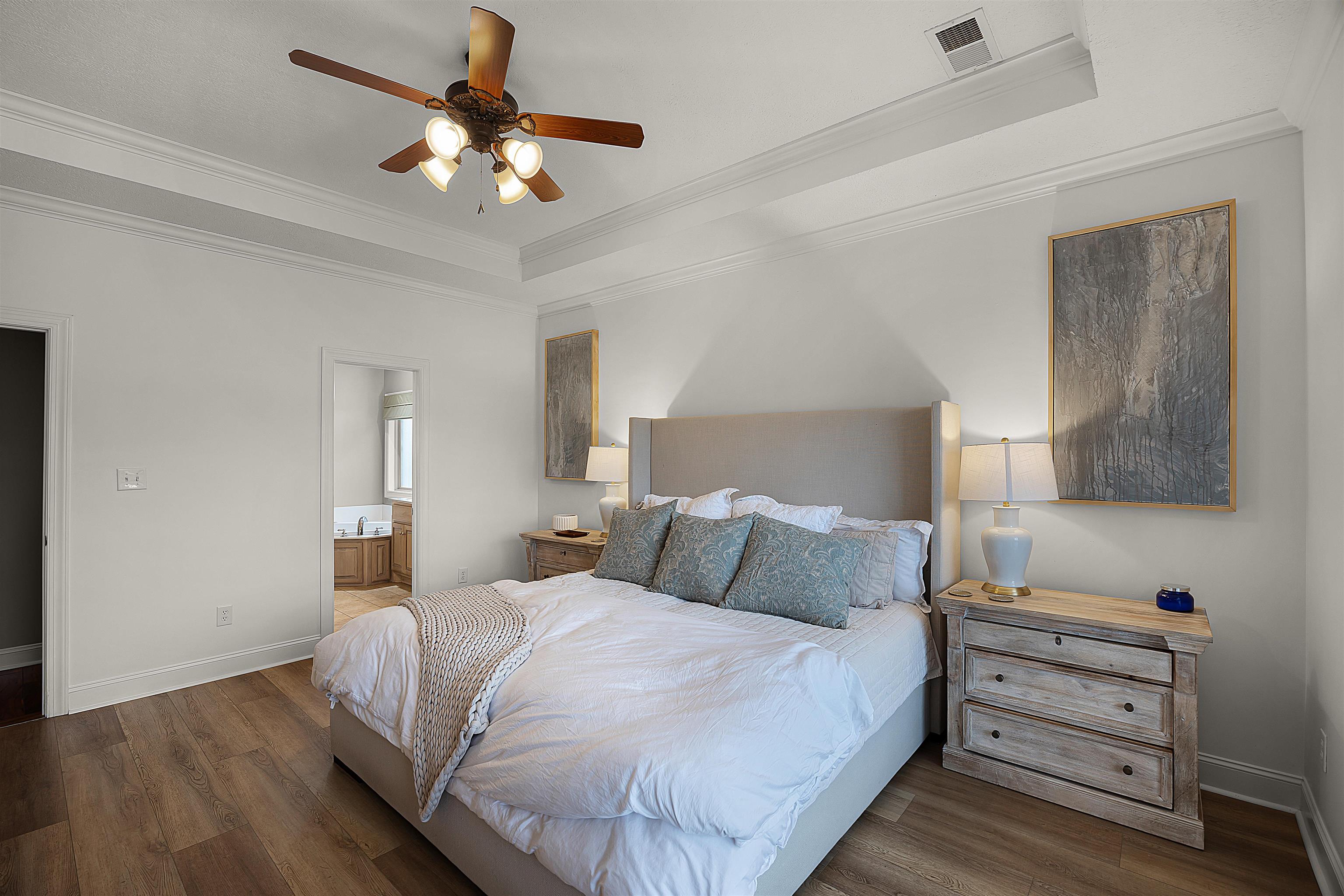 Bedroom with crown molding, ceiling fan, dark hardwood / wood-style floors, a raised ceiling, and ensuite bath