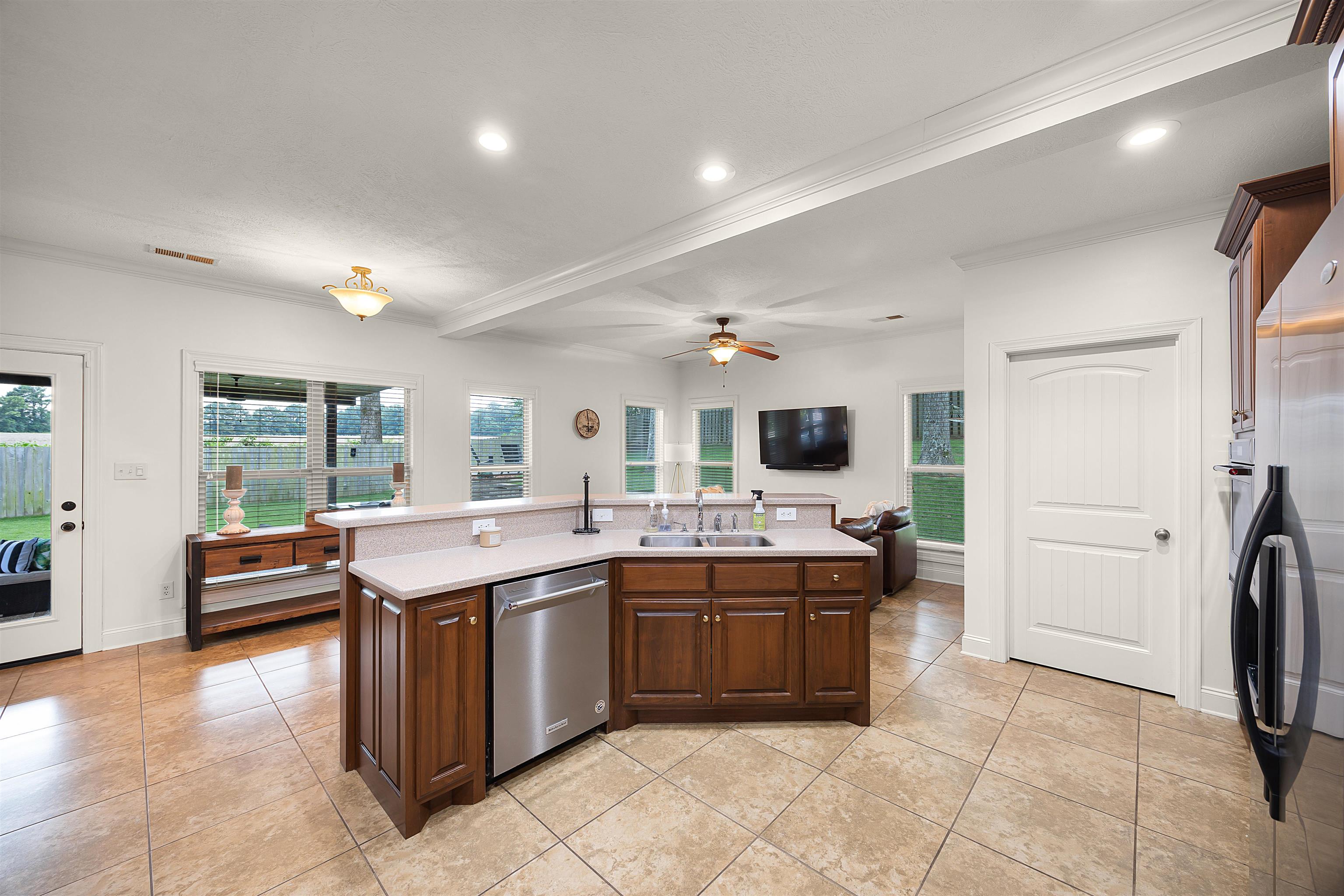 Kitchen featuring a center island with sink, light tile patterned floors, dishwasher, ceiling fan, and ornamental molding