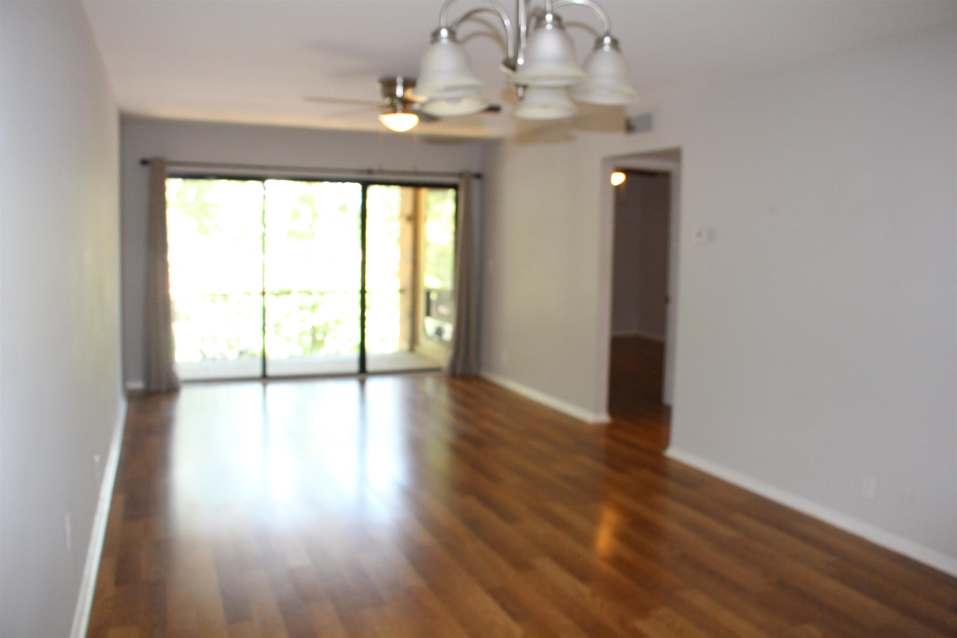 Empty room featuring dark hardwood / wood-style flooring and ceiling fan with notable chandelier