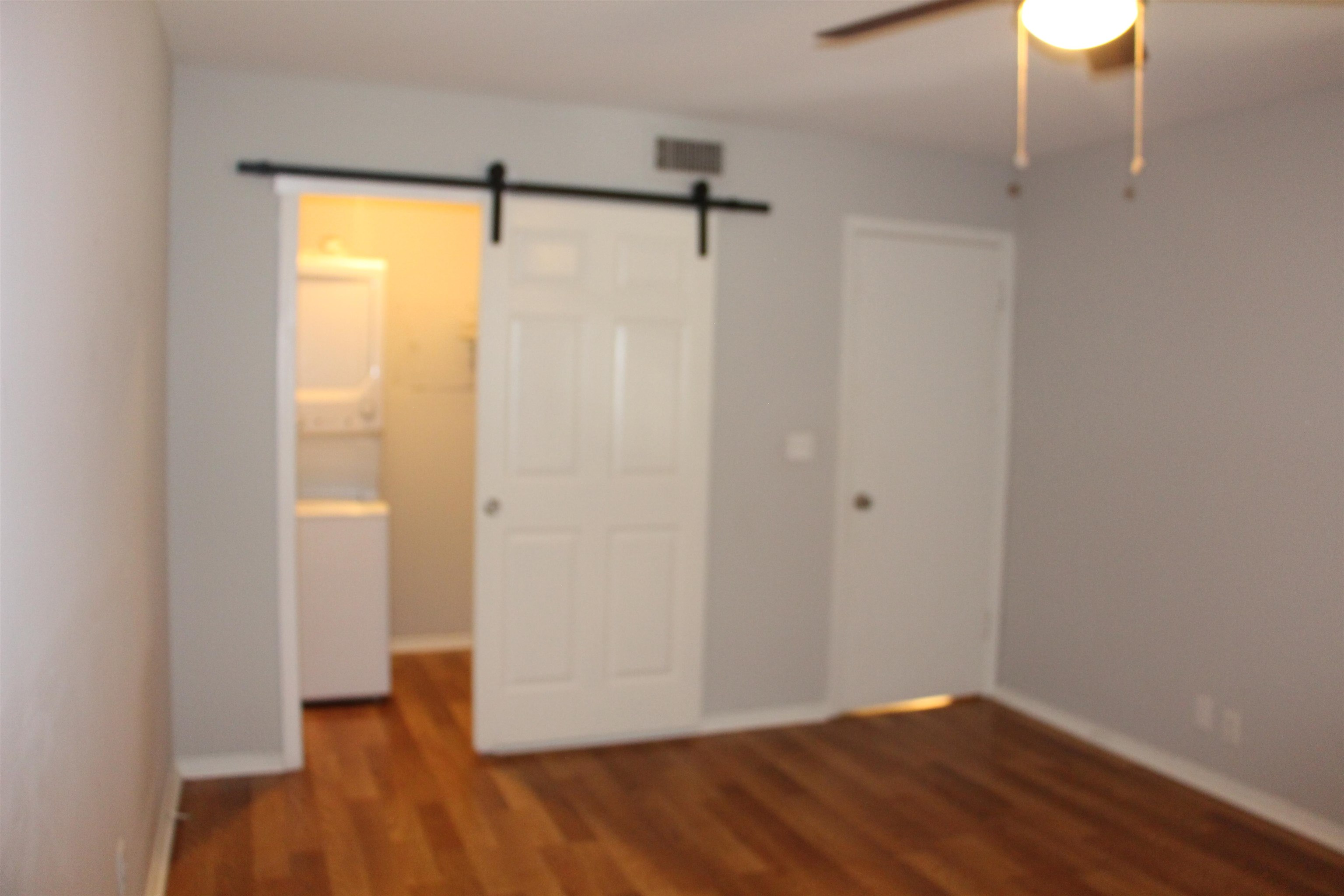 Unfurnished bedroom with ceiling fan, connected bathroom, wood-type flooring, and a barn door