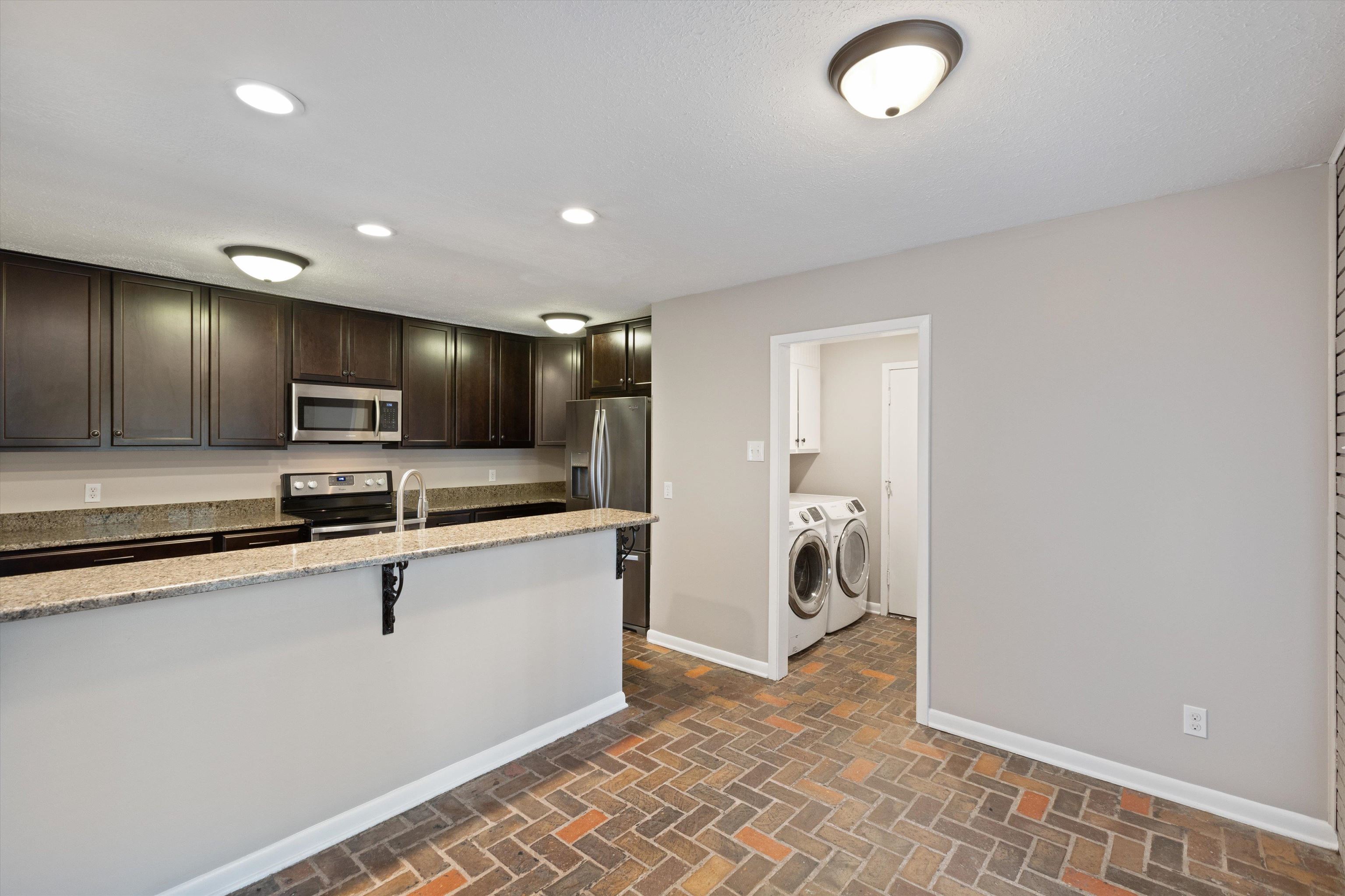 Kitchen with stainless steel appliances, a breakfast bar, washer and clothes dryer, dark brown cabinetry, and light stone countertops