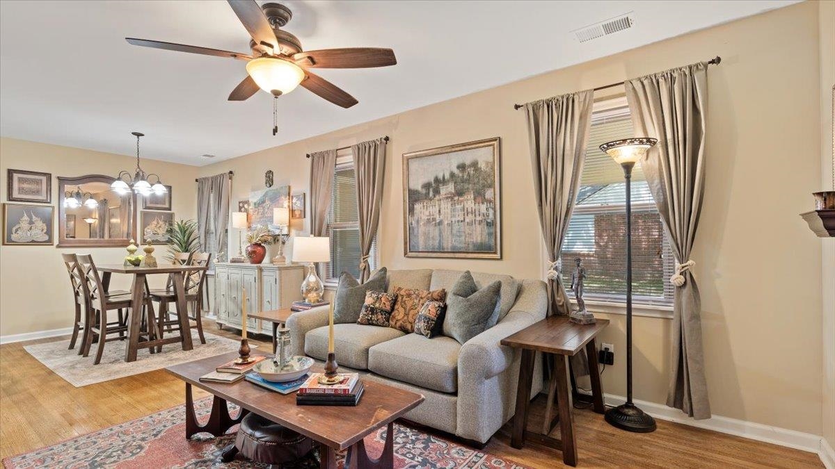 Living room with wood-type flooring and ceiling fan with notable chandelier