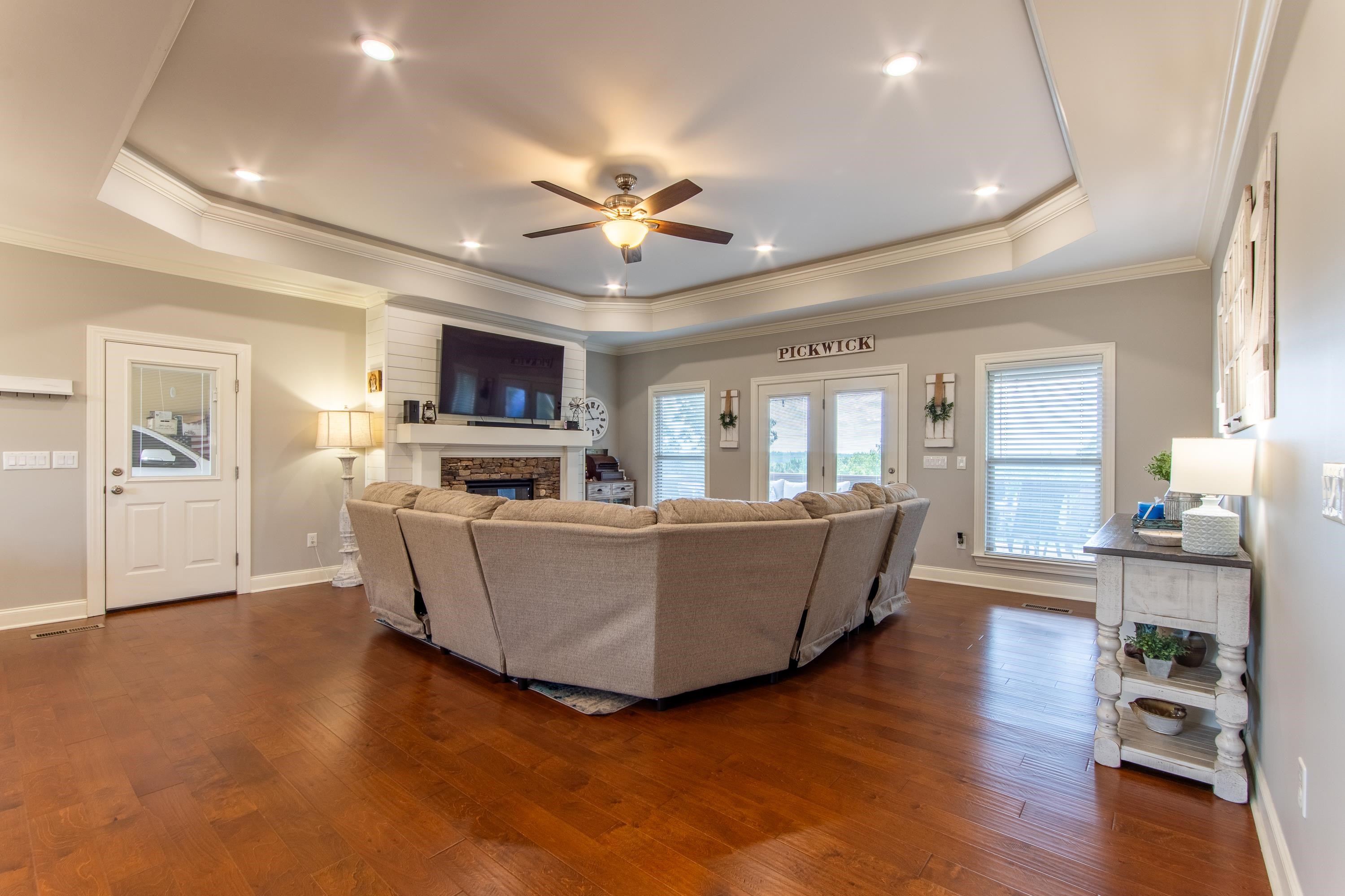 Living room featuring dark wood-type flooring, ceiling fan, a fireplace, a raised ceiling, and ornamental molding