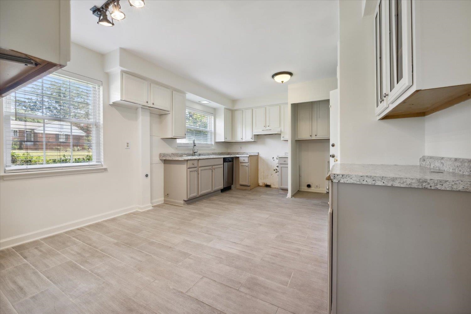 Kitchen featuring gray cabinets, stainless steel dishwasher, and light stone countertops