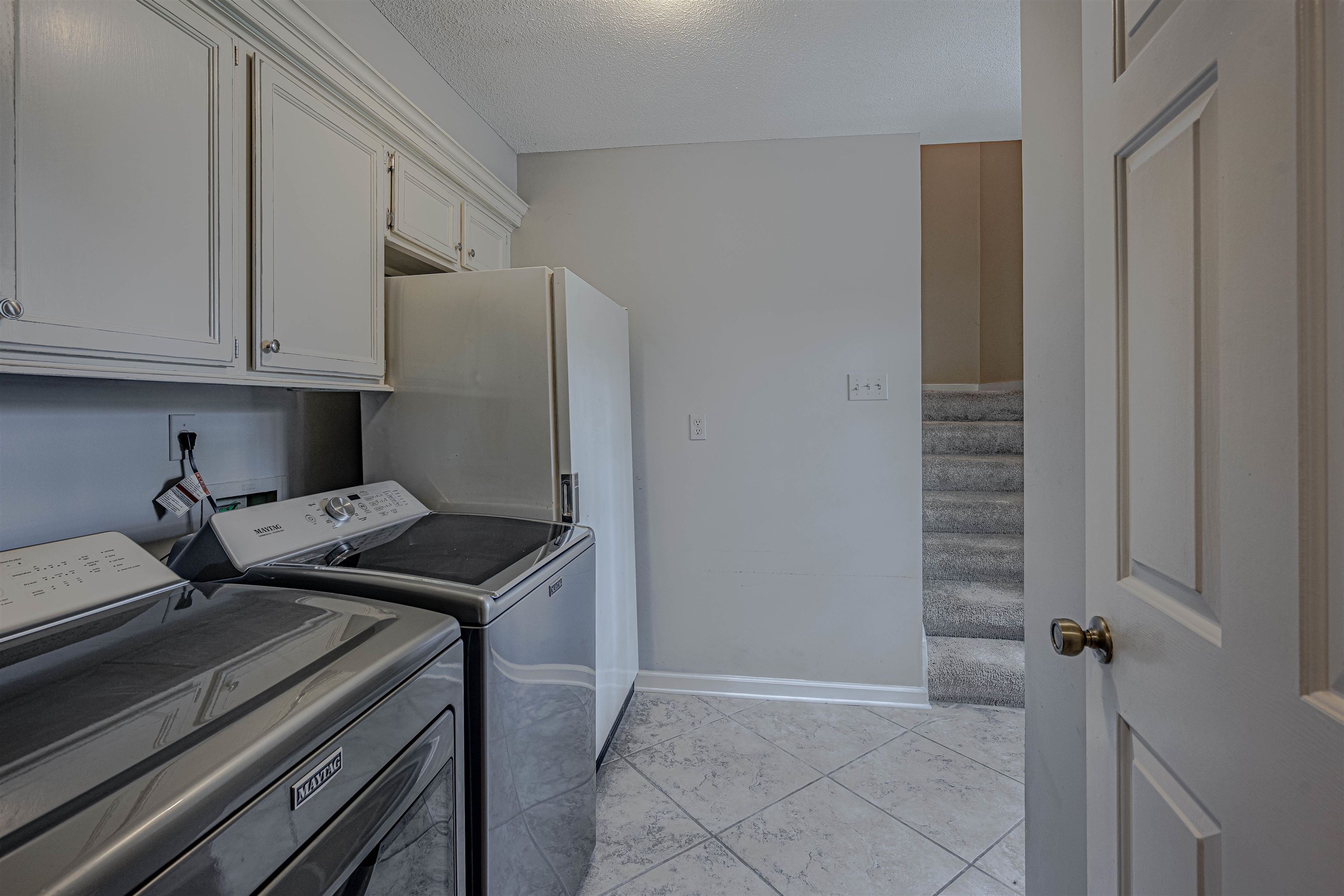 Clothes washing area with light tile patterned flooring, cabinets, and washer and dryer