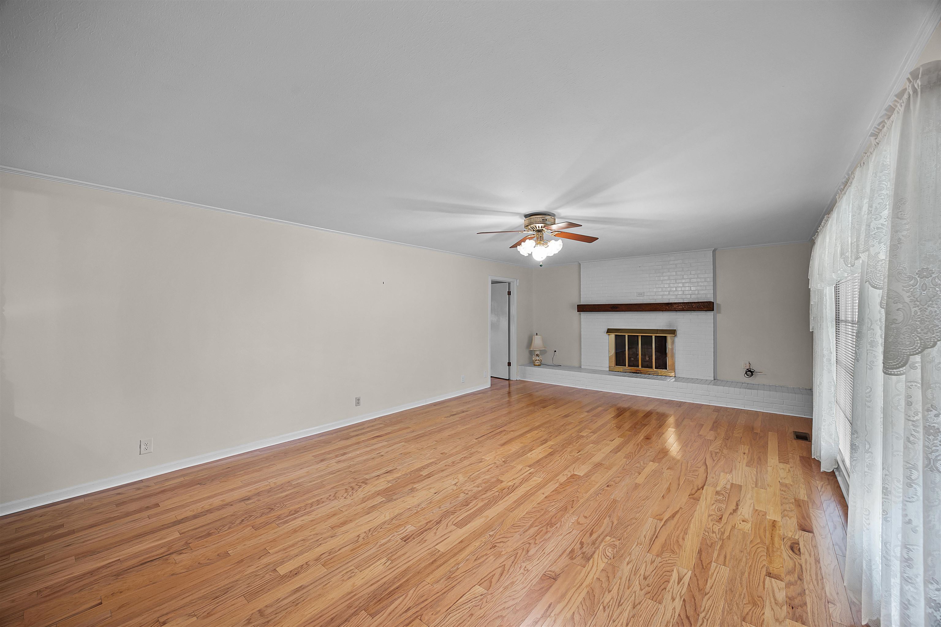 Unfurnished living room featuring brick wall, light hardwood / wood-style flooring, a fireplace, and ceiling fan