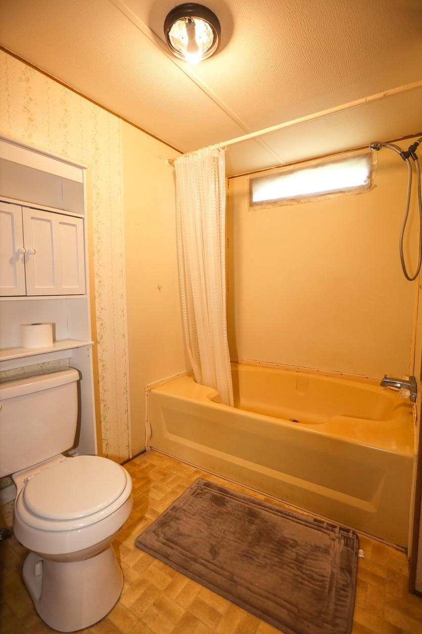 Bathroom featuring toilet and shower / bathtub combination with curtain