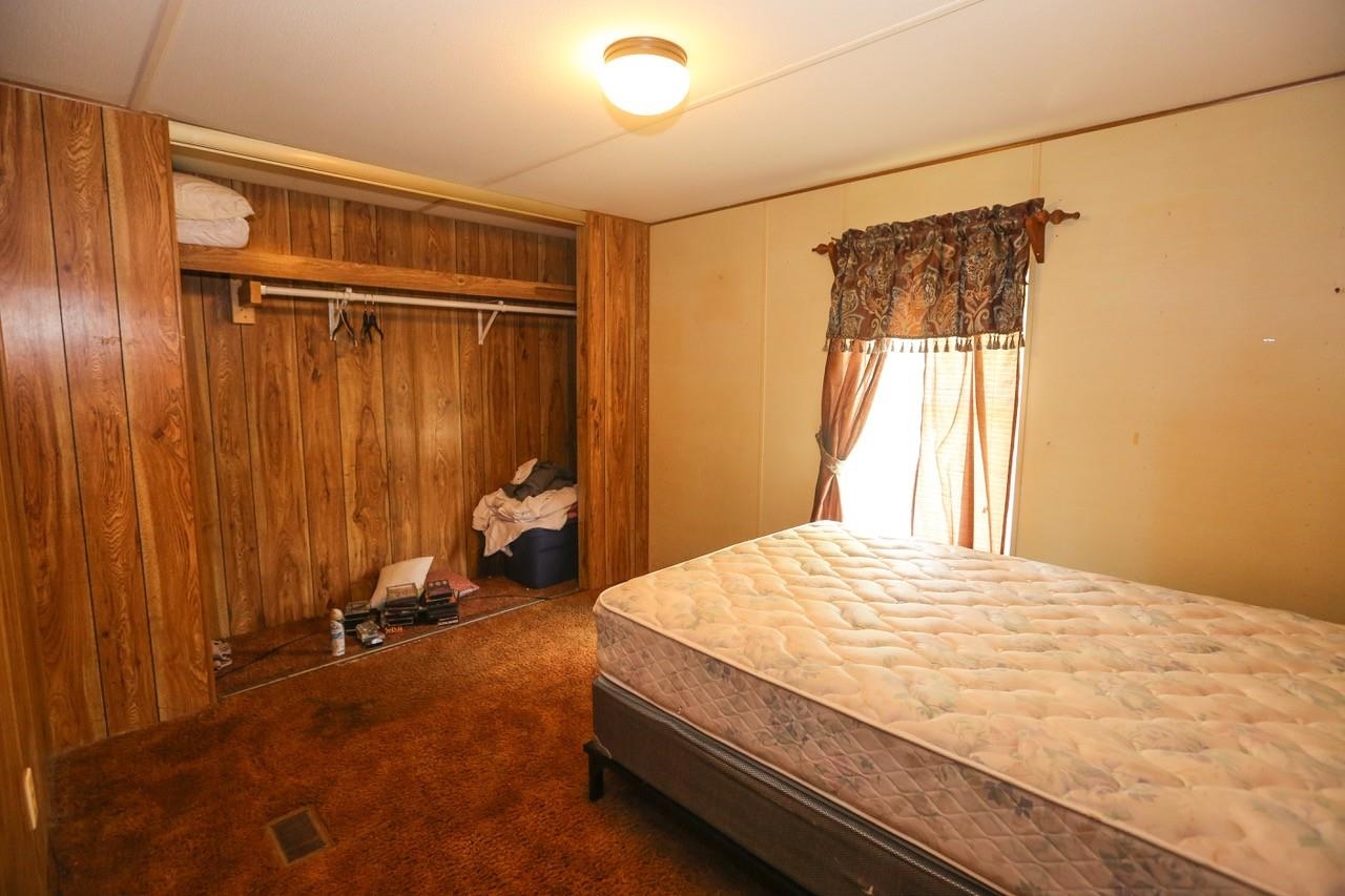 Bedroom with carpet floors, wooden walls, and a closet