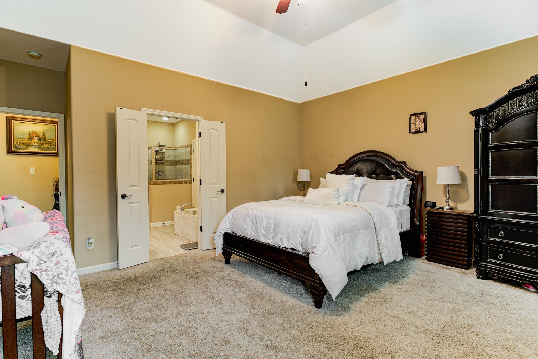 Bedroom with light carpet, ensuite bathroom, and ceiling fan