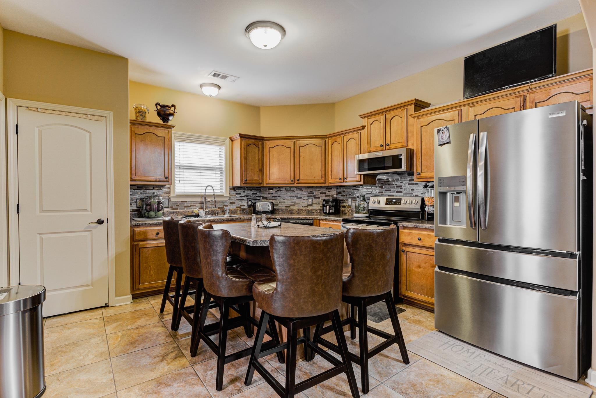 Kitchen with light tile patterned flooring, a center island, tasteful backsplash, and stainless steel appliances