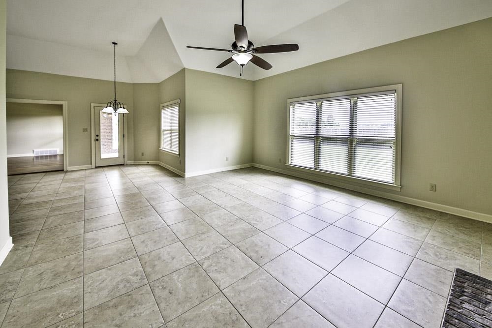 Unfurnished living room featuring light tile patterned flooring, ceiling fan with notable chandelier, and a healthy amount of sunlight