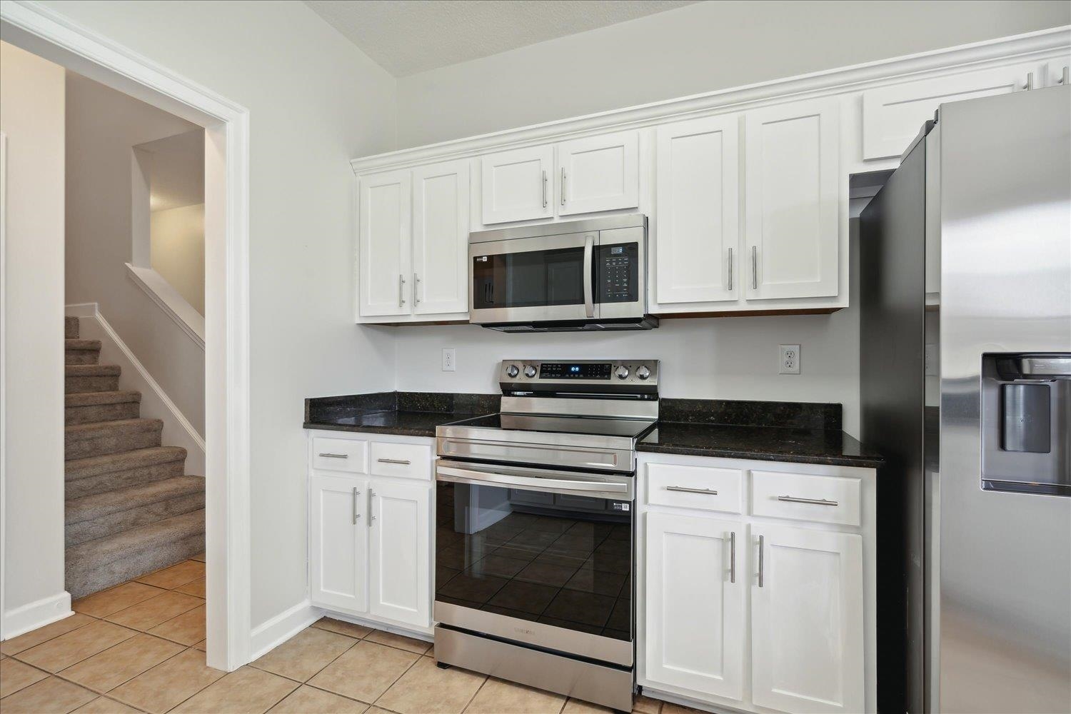 Kitchen featuring dark stone counters, stainless steel appliances, light tile patterned floors, and white cabinets