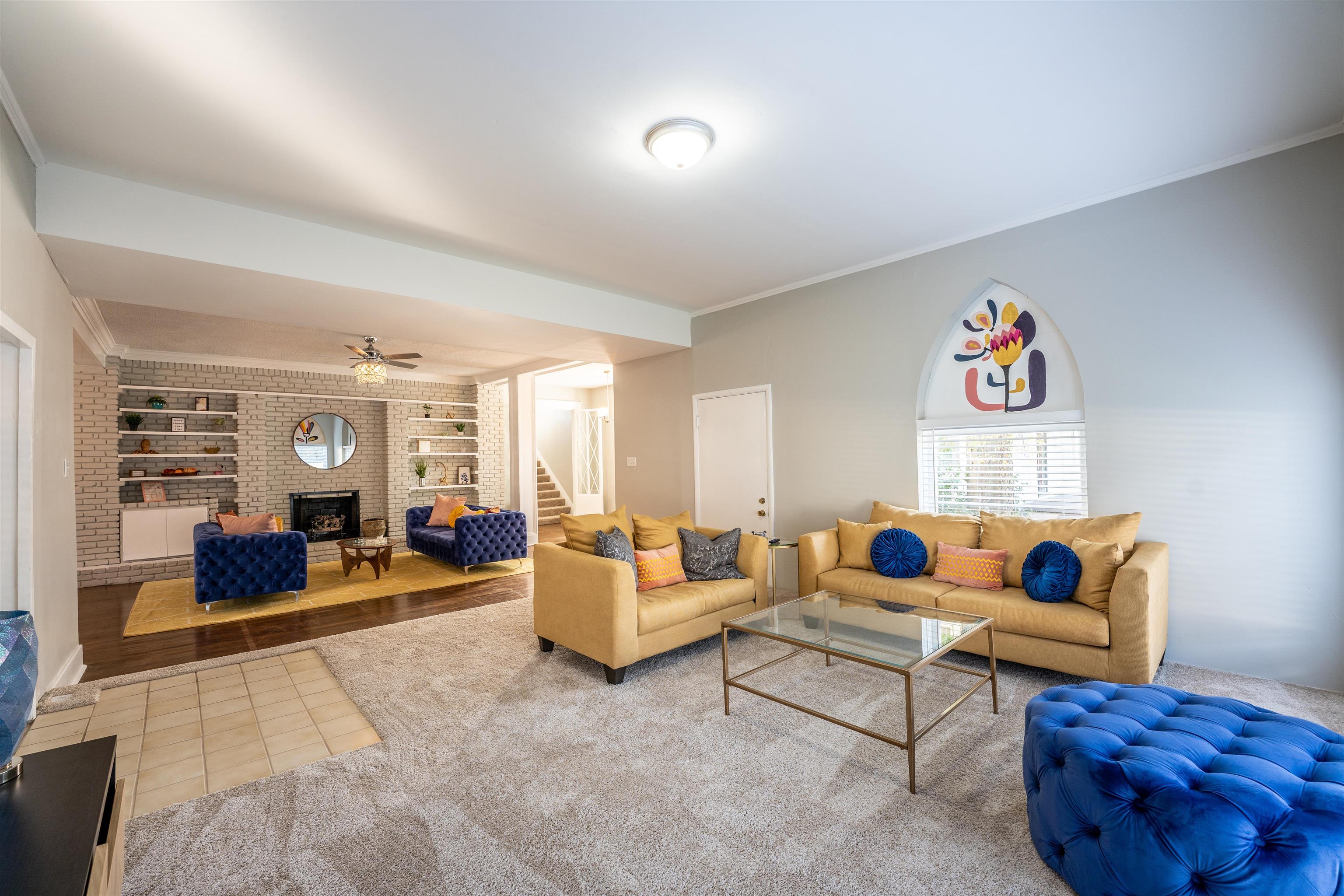 Living room with built in shelves, ceiling fan, tile patterned floors, a brick fireplace, and ornamental molding