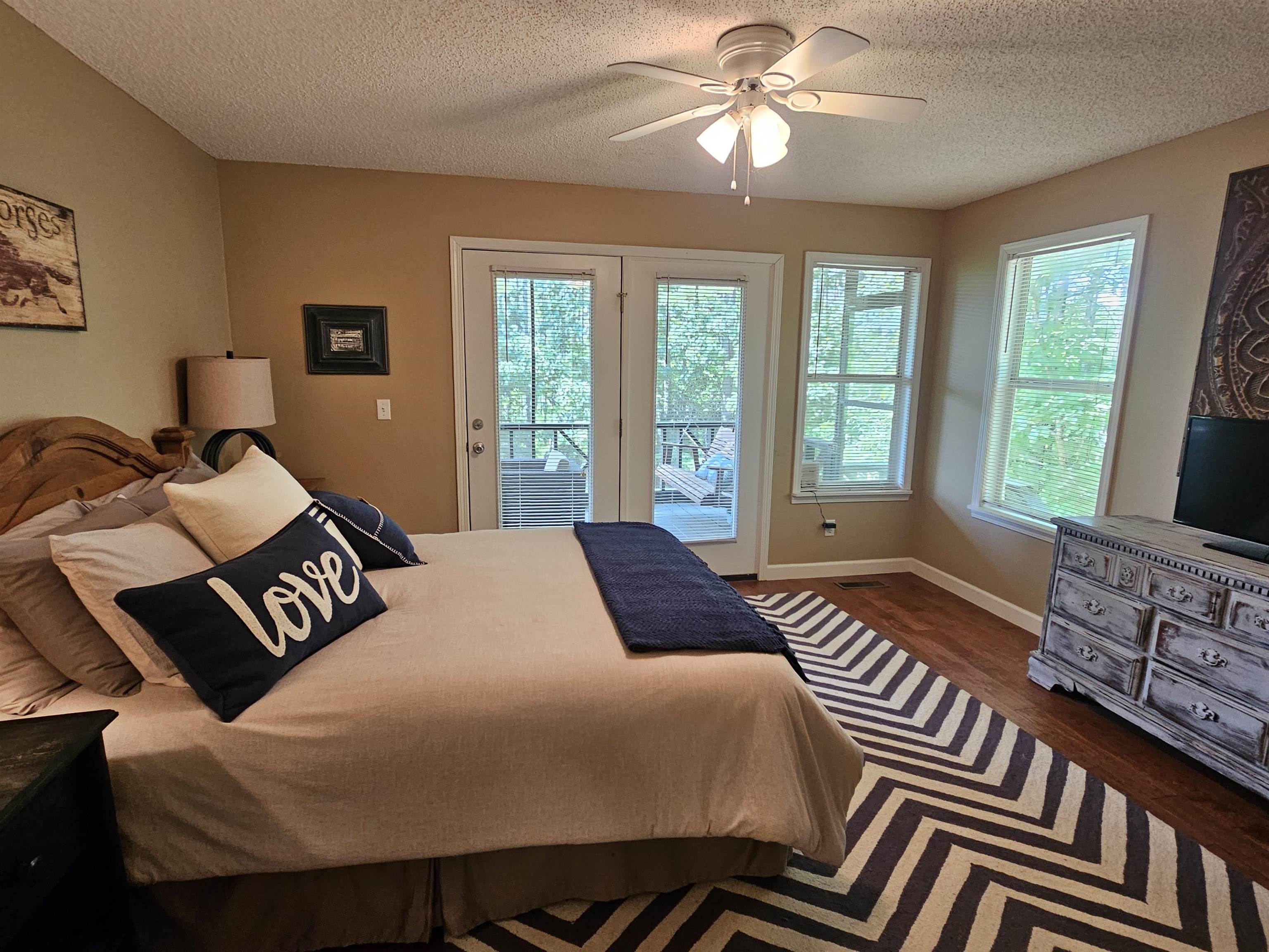 Bedroom with multiple windows, access to outside, dark hardwood / wood-style floors, and ceiling fan