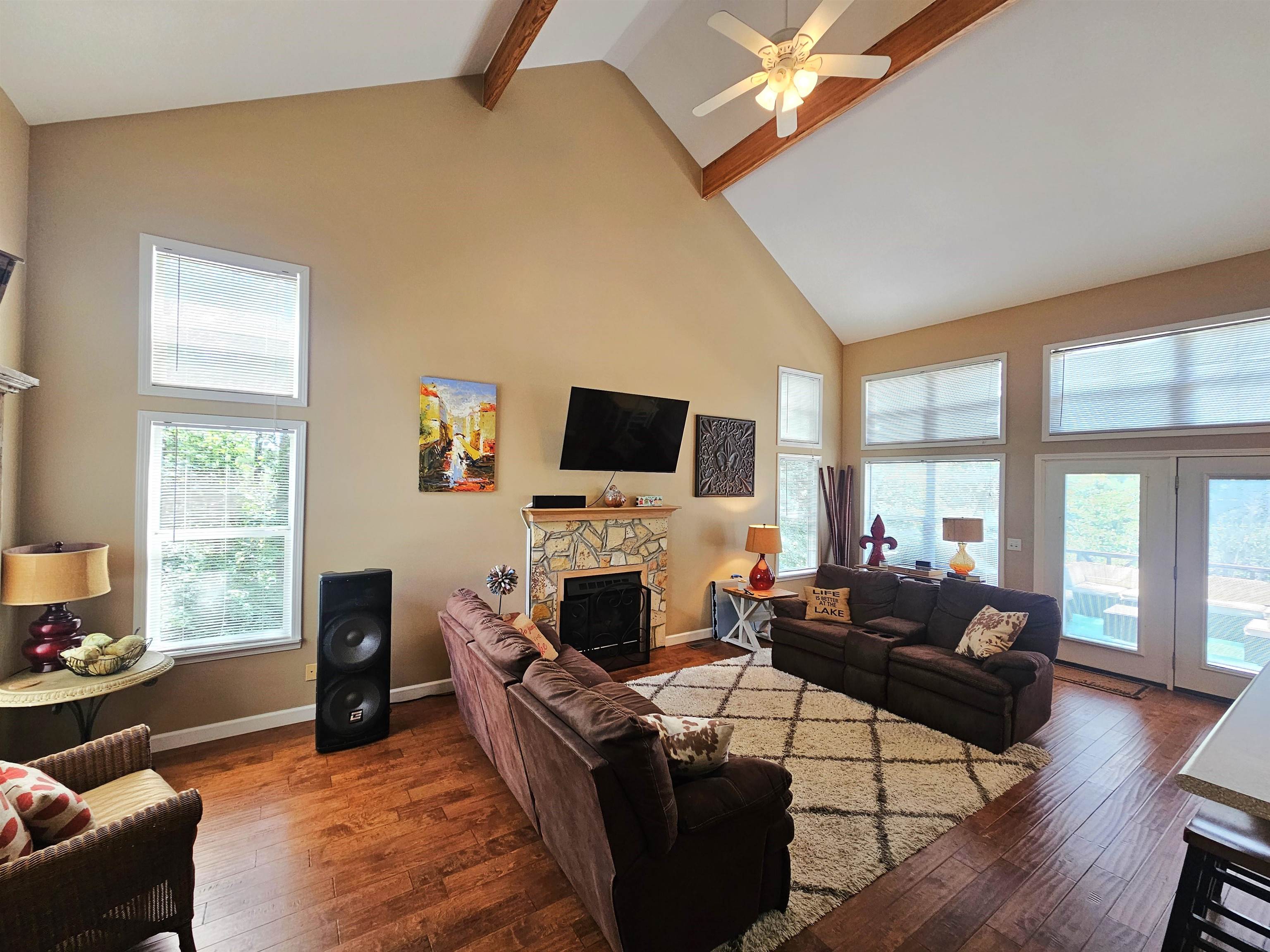 Living room featuring beamed ceiling, a fireplace, dark hardwood / wood-style flooring, high vaulted ceiling, and ceiling fan