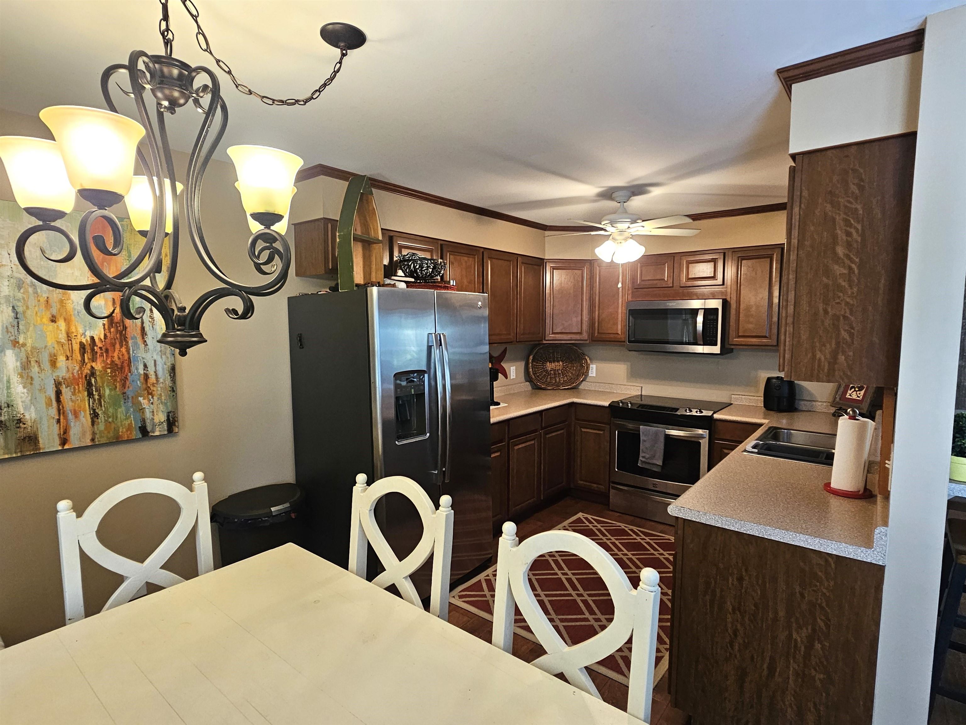 Kitchen with decorative light fixtures, stainless steel appliances, ceiling fan with notable chandelier, crown molding, and sink