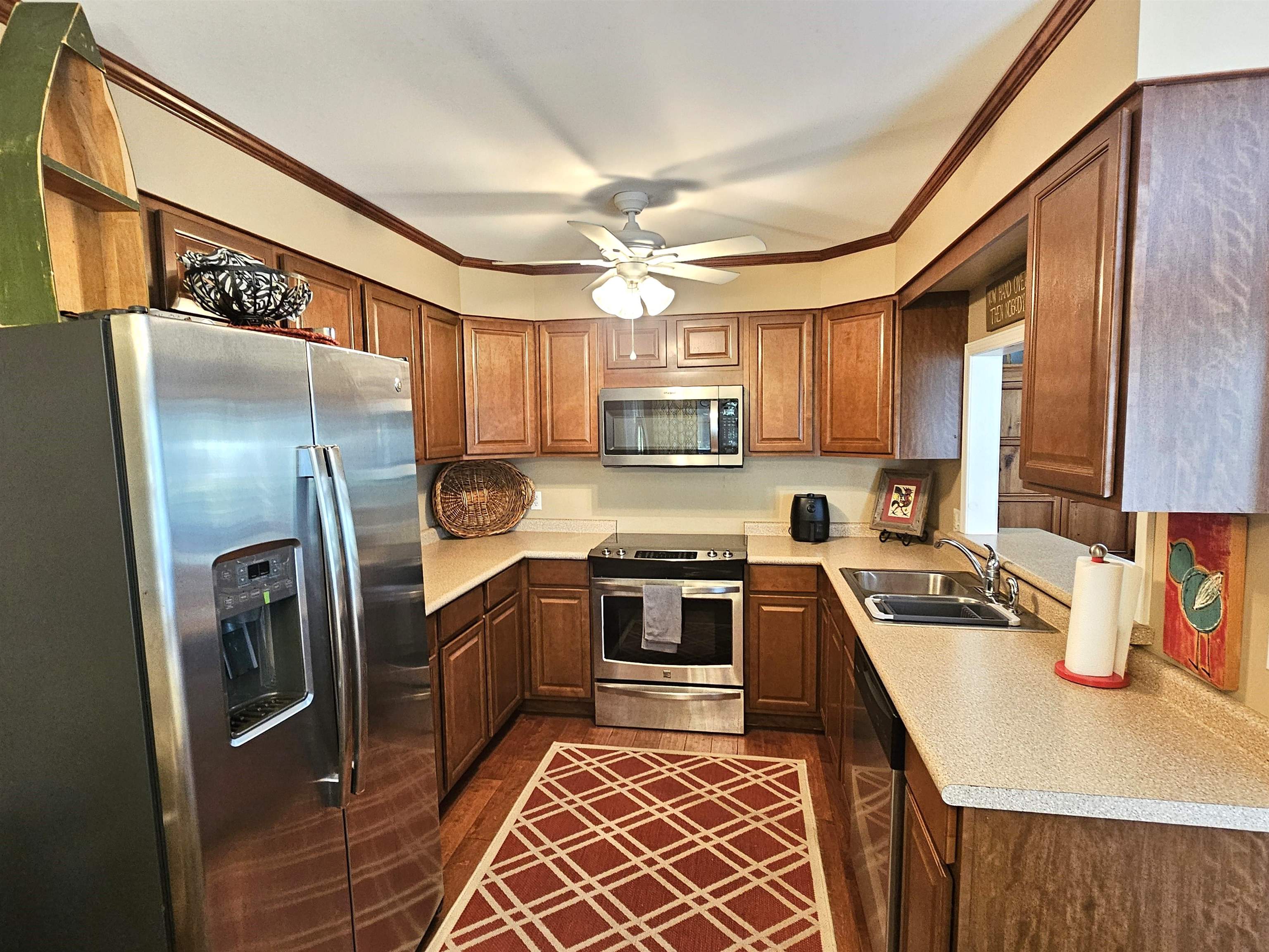 Kitchen with stainless steel appliances, sink, dark hardwood / wood-style flooring, ceiling fan, and ornamental molding