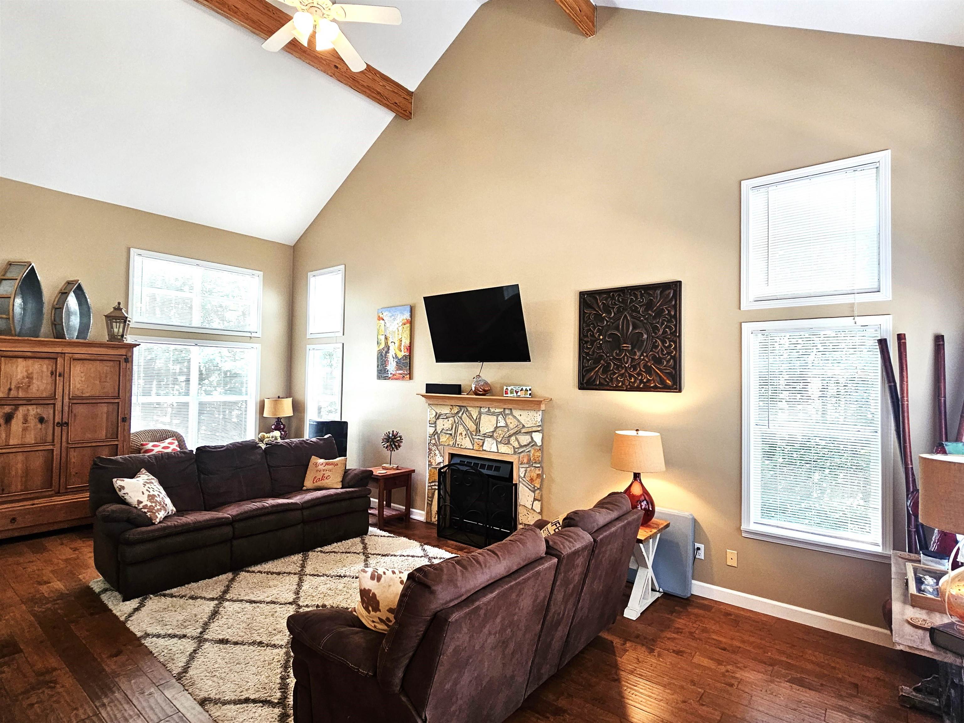 Living room featuring a stone fireplace, dark hardwood / wood-style flooring, and beam ceiling