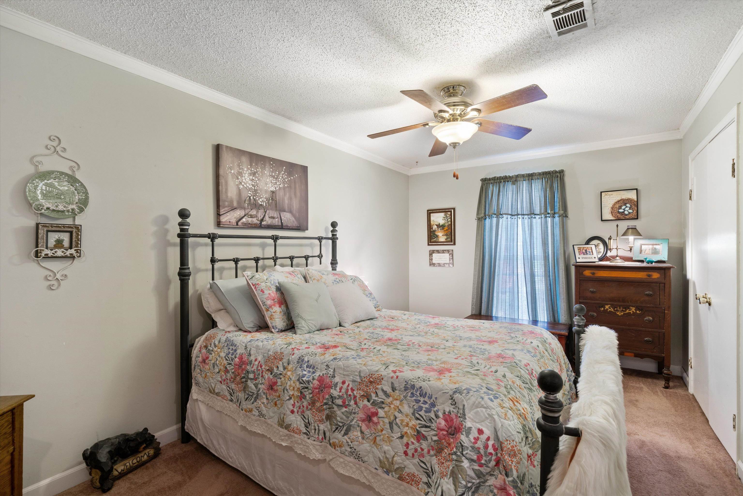 Carpeted bedroom with a textured ceiling, ceiling fan, and ornamental molding