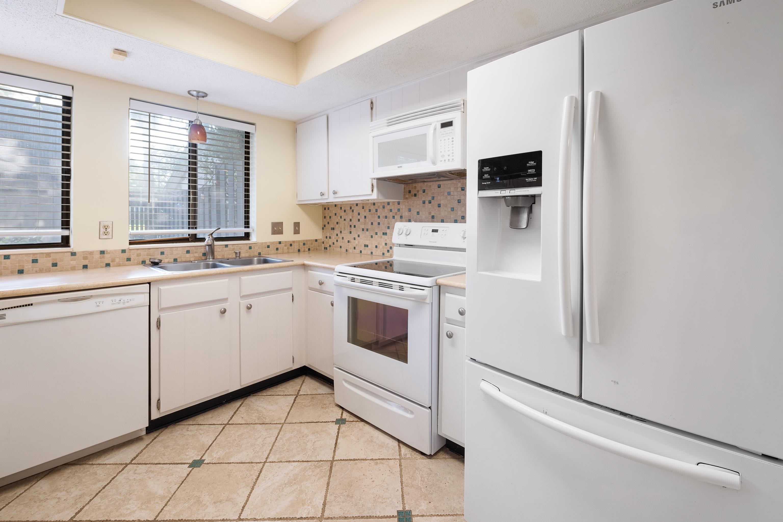 Kitchen featuring white cabinetry, white appliances, light tile patterned floors, backsplash, and sink