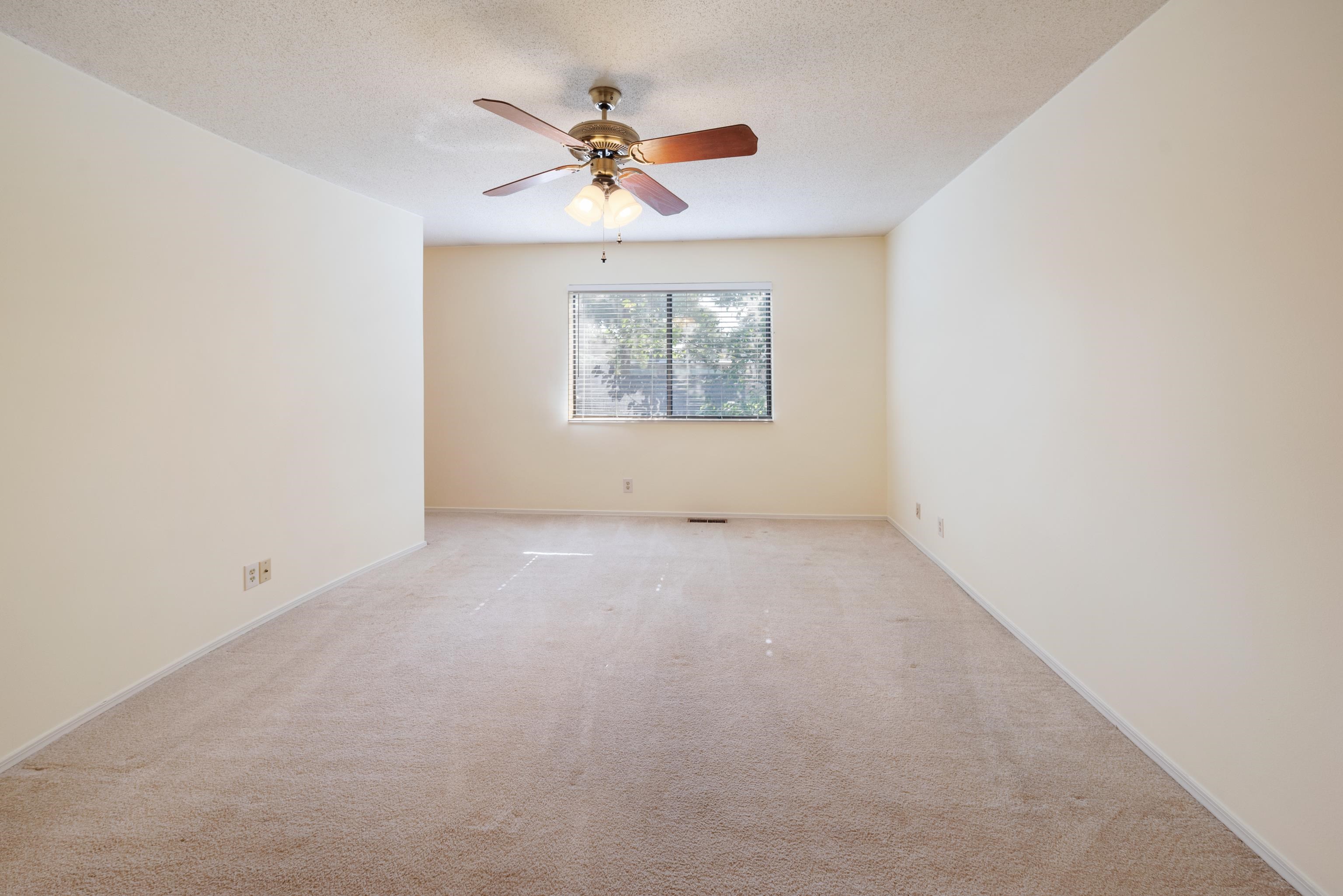 Primary bedroom with a textured ceiling, light colored carpet, and ceiling fan