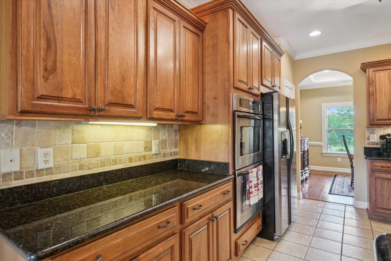 Kitchen featuring dark stone counters, stainless steel appliances, crown molding, light hardwood / wood-style floors, and backsplash